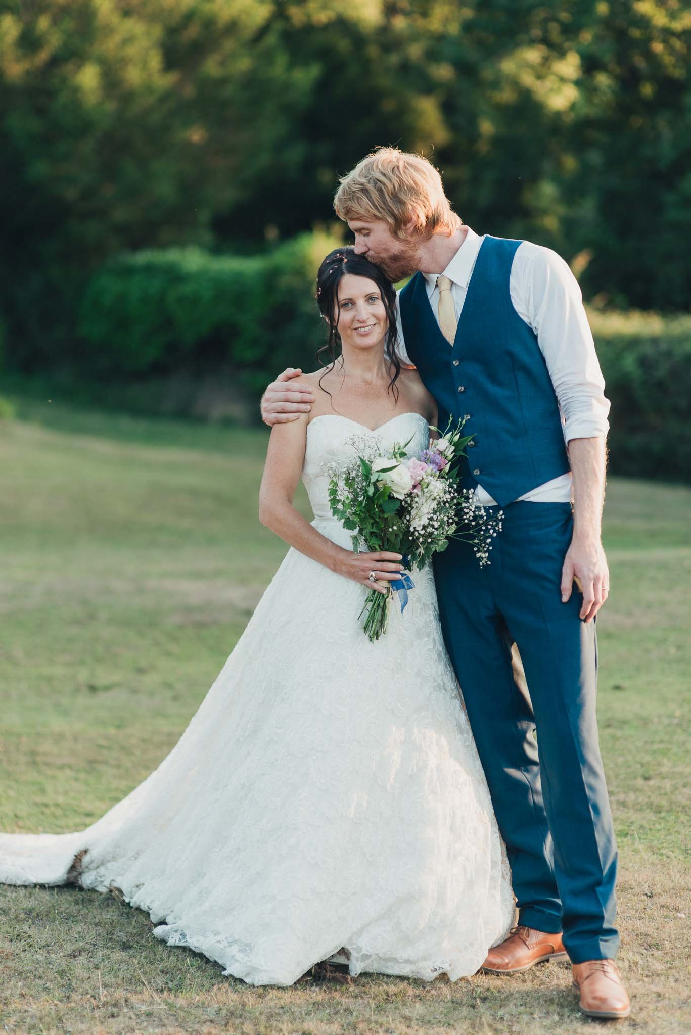 The bride and groom standing together outdoors for a portrait, holding the bouquet.