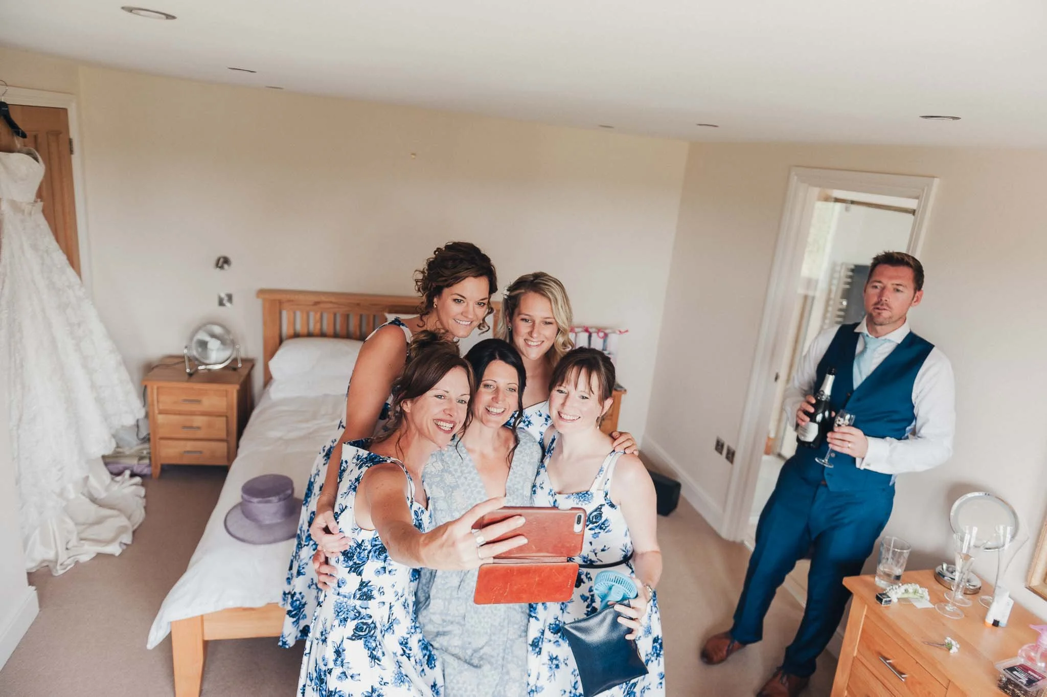 The bride and bridesmaids gathered on the bed taking a group selfie while getting ready.