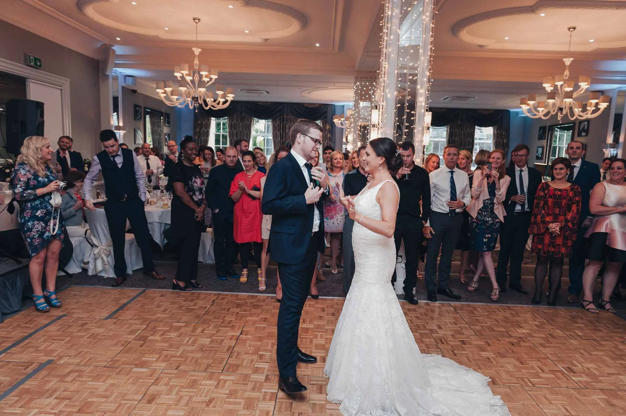 The couple sharing their first dance on the ballroom floor while guests gather around.