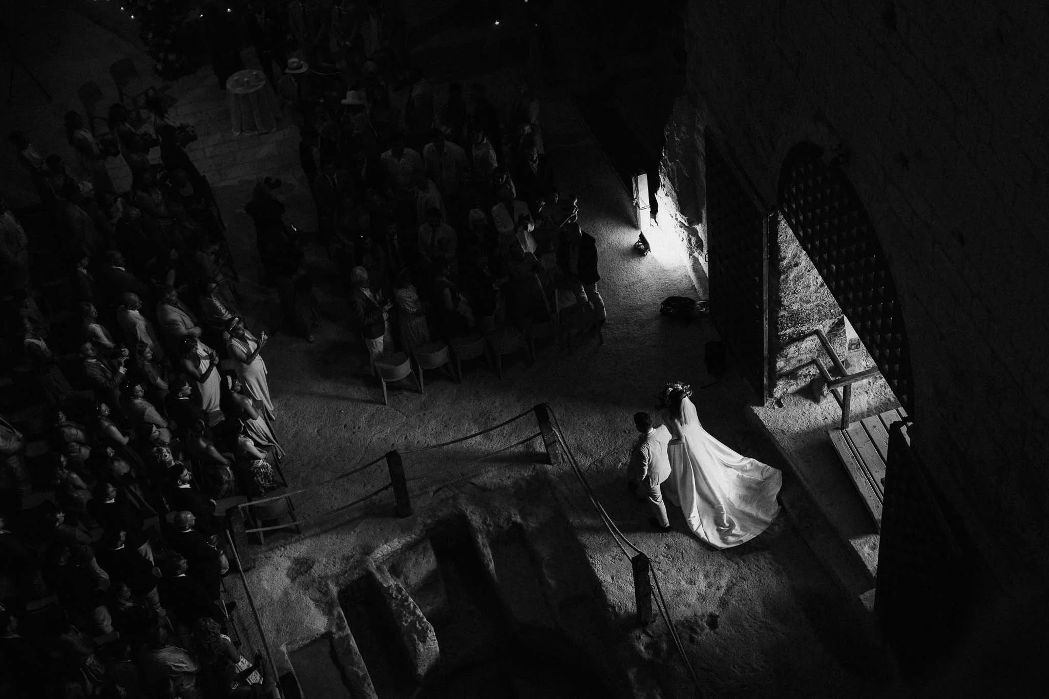 Black-and-white overhead view of the bride entering the Église Souterraine Saint-Jean in Aubeterre-sur-Dronne.