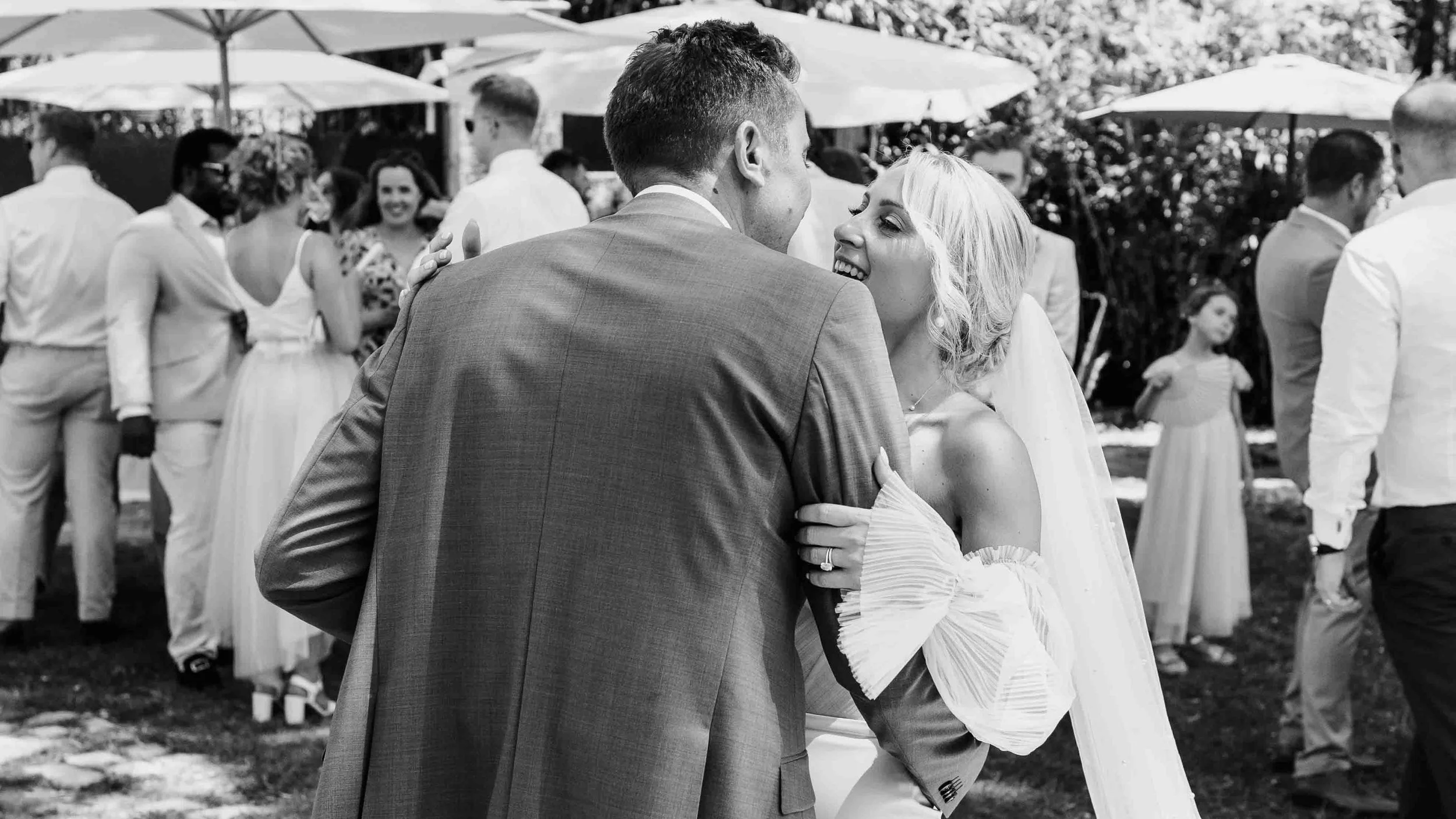 Bride and groom sharing a laugh during the reception, surrounded by guests under parasols