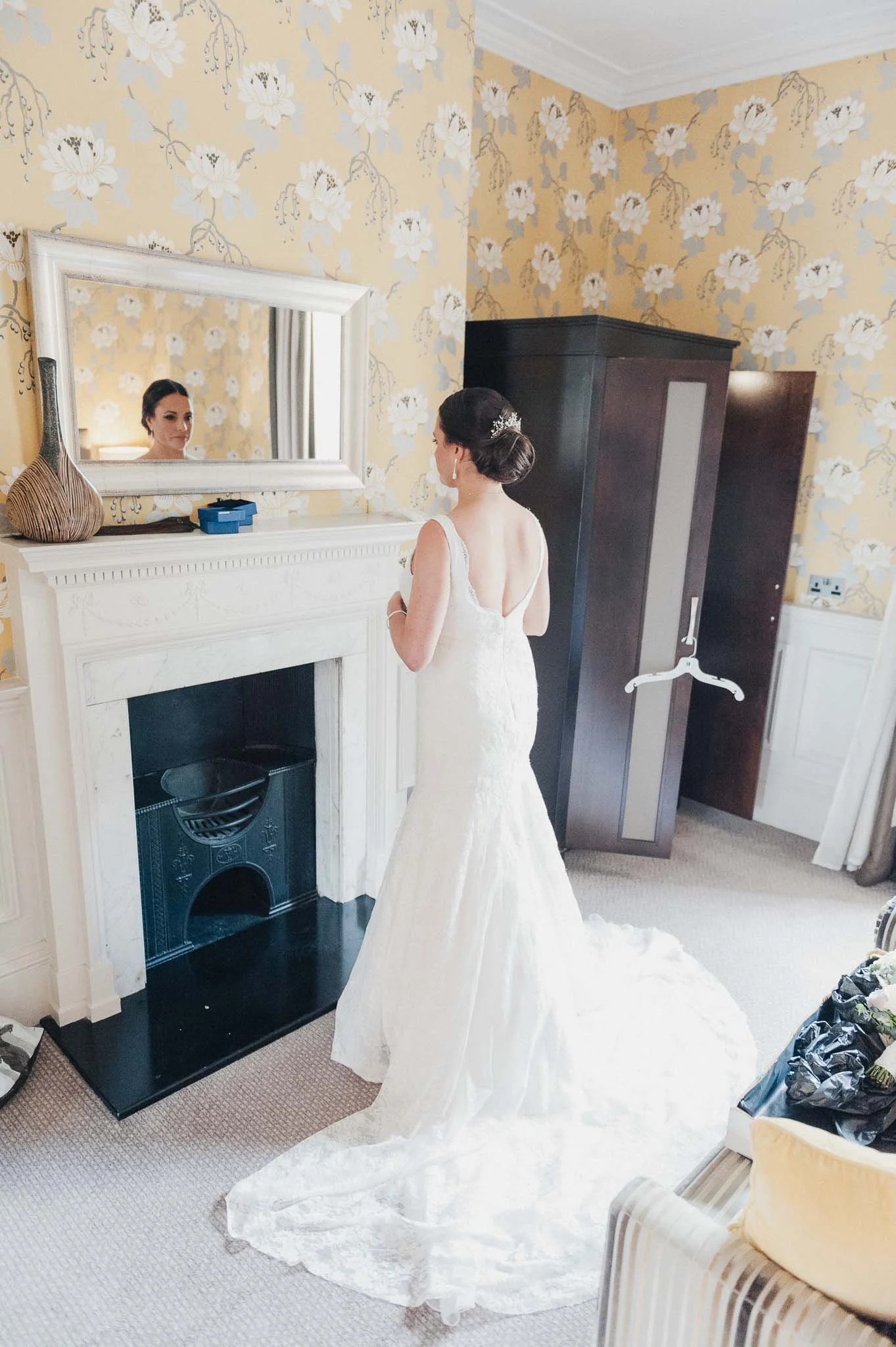 Bride adjusting the back of her dress while standing near the fireplace before the ceremony.