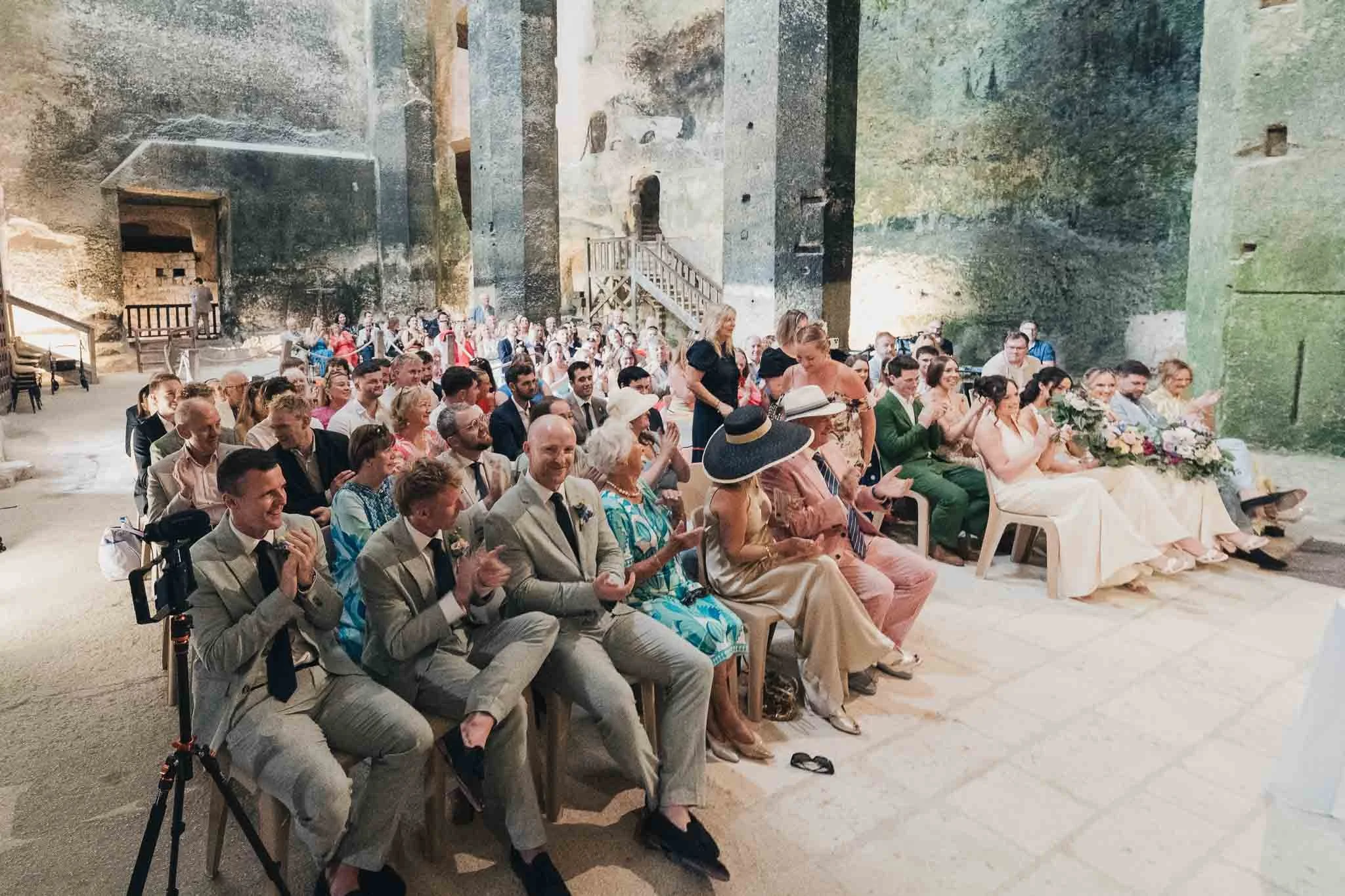 Guests seated inside the Église Souterraine Saint-Jean, clapping during the ceremony.