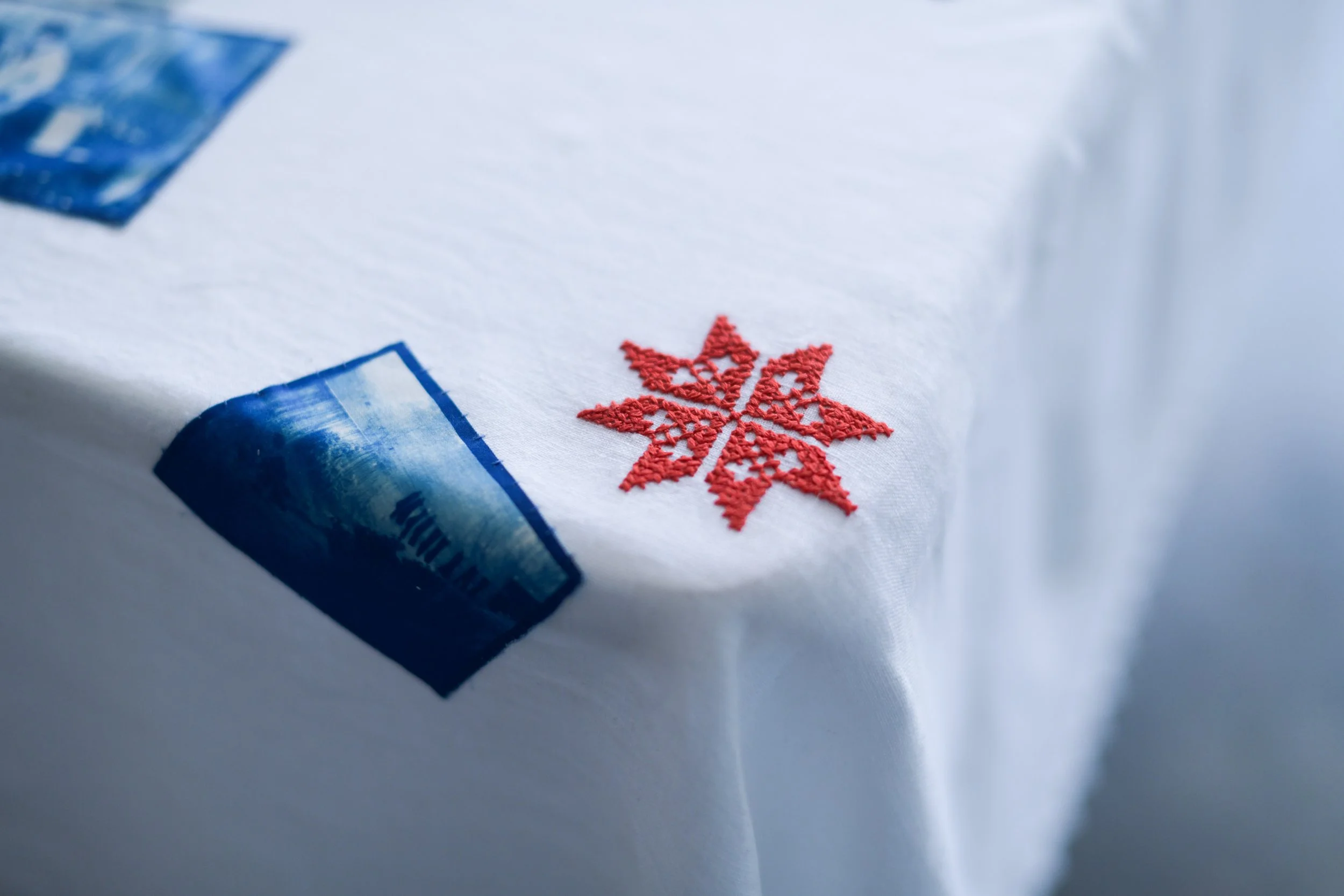 Close-up of a white fabric with a red embroidered snowflake design and a partially visible blue and white label.