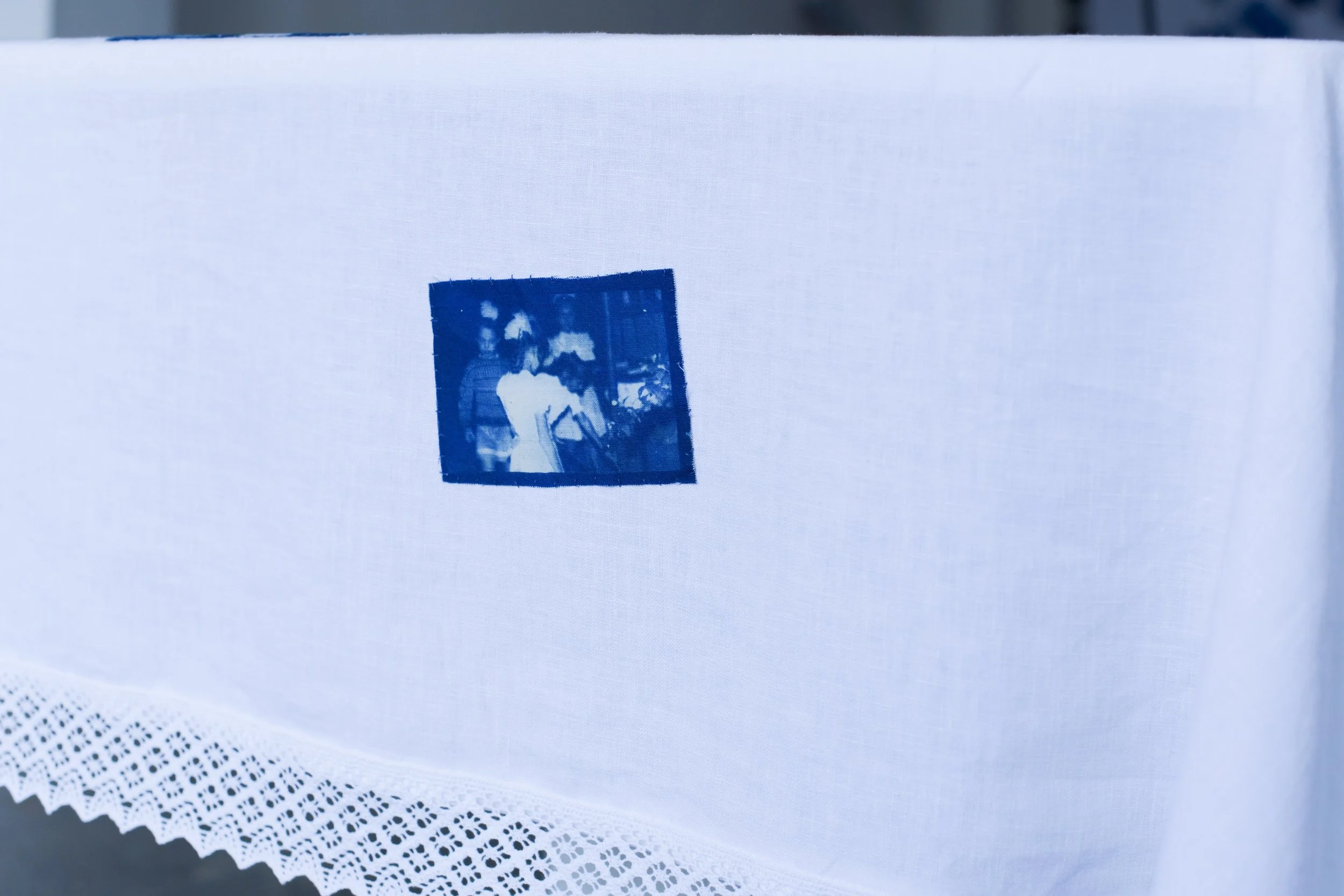 White fabric surface with a small blue stamp of a framed black and white photograph, and a patterned paper with a lace-like edge in the foreground.