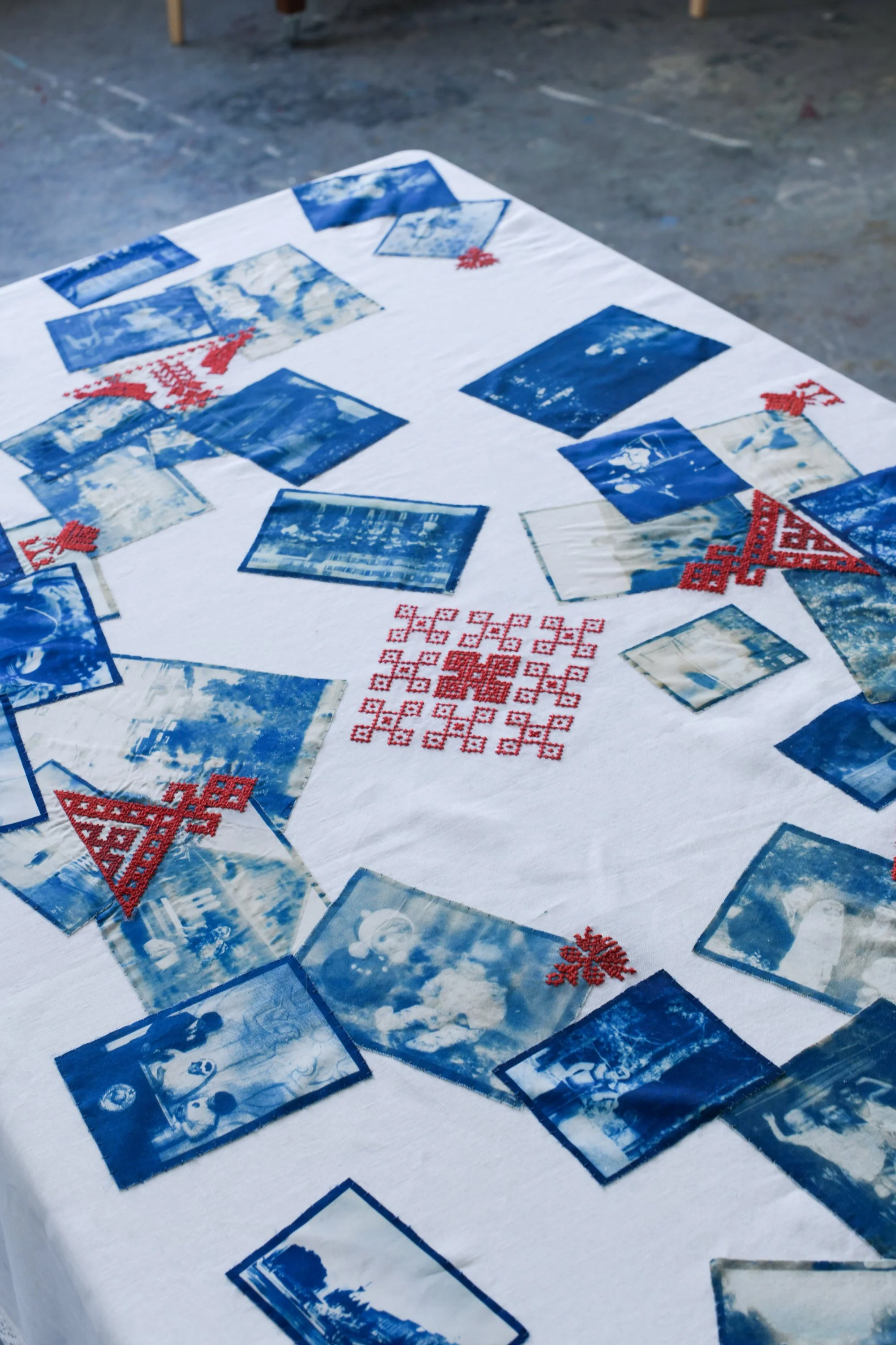A table covered with a white cloth displaying several blue and white landscape photographs and red embroidered decorations.