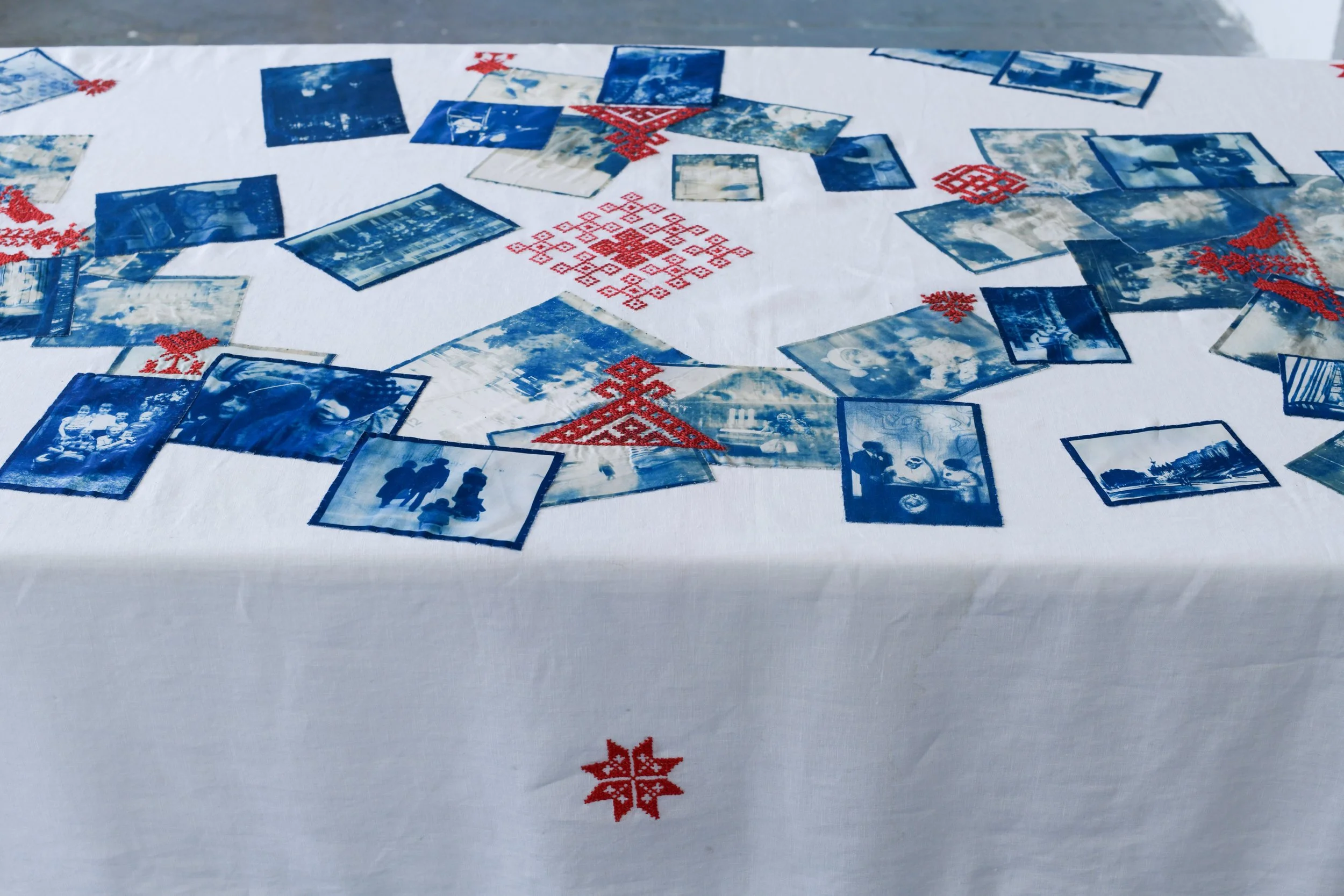 A tablecloth with Christmas-themed red embroidered snowflakes and holly, decorated with old black-and-white and blue photographs spread out across the surface.