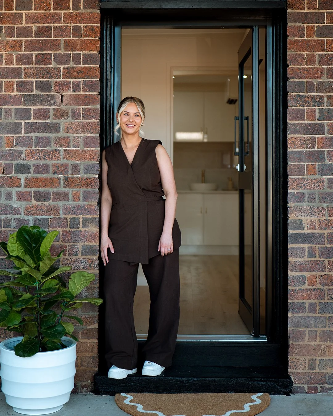 Photo of Letitia, owner of Letitia Aesthetics leaning against a brick wall