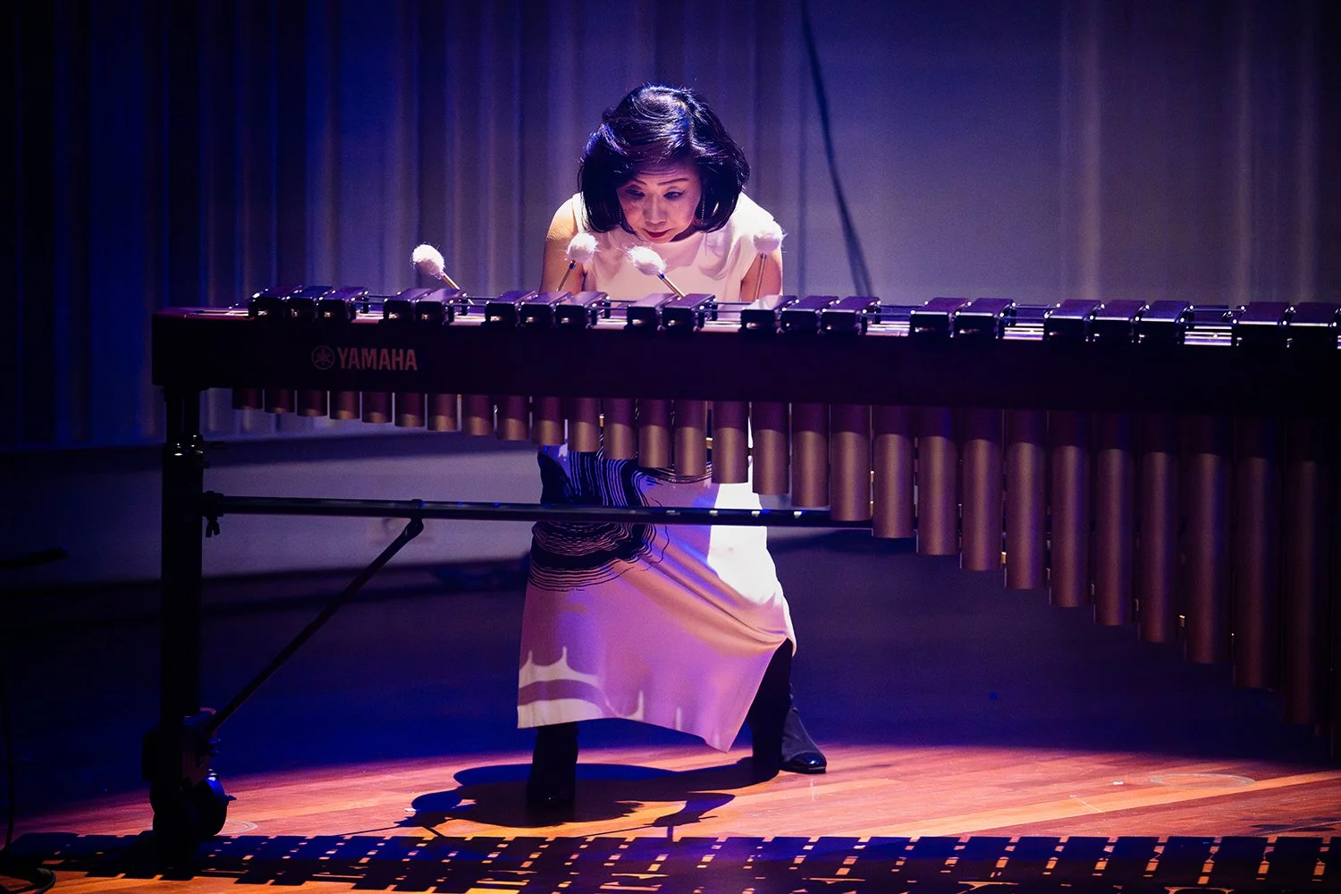Woman playing Yamaha marimba on stage, illuminated by purple stage lighting.