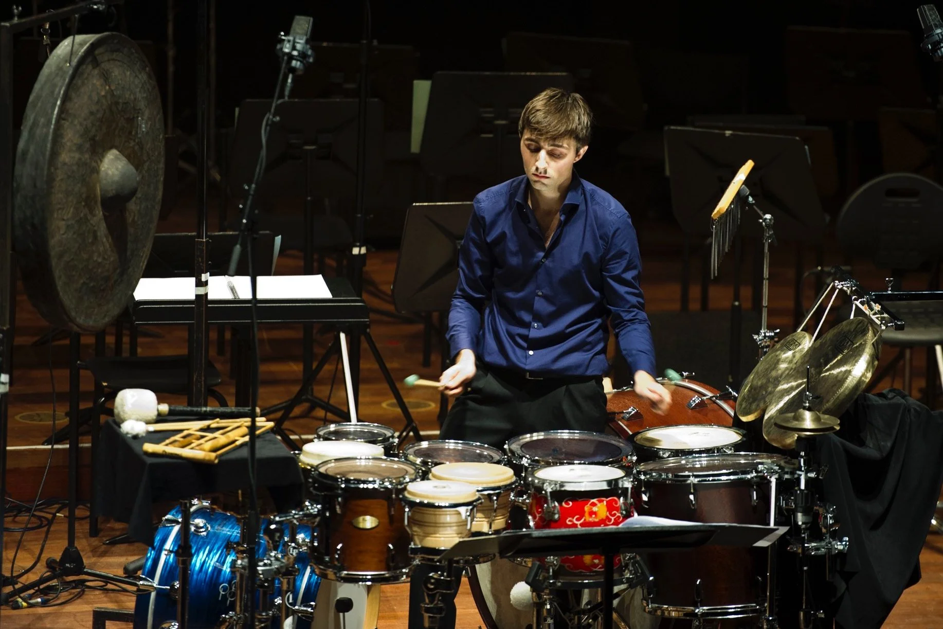Dominique Vleeshouwers playing a setup piece during the final of the Tromp Percussion Eindhoven 2014 competition with various drums, cymbals, and gongs on a stage.