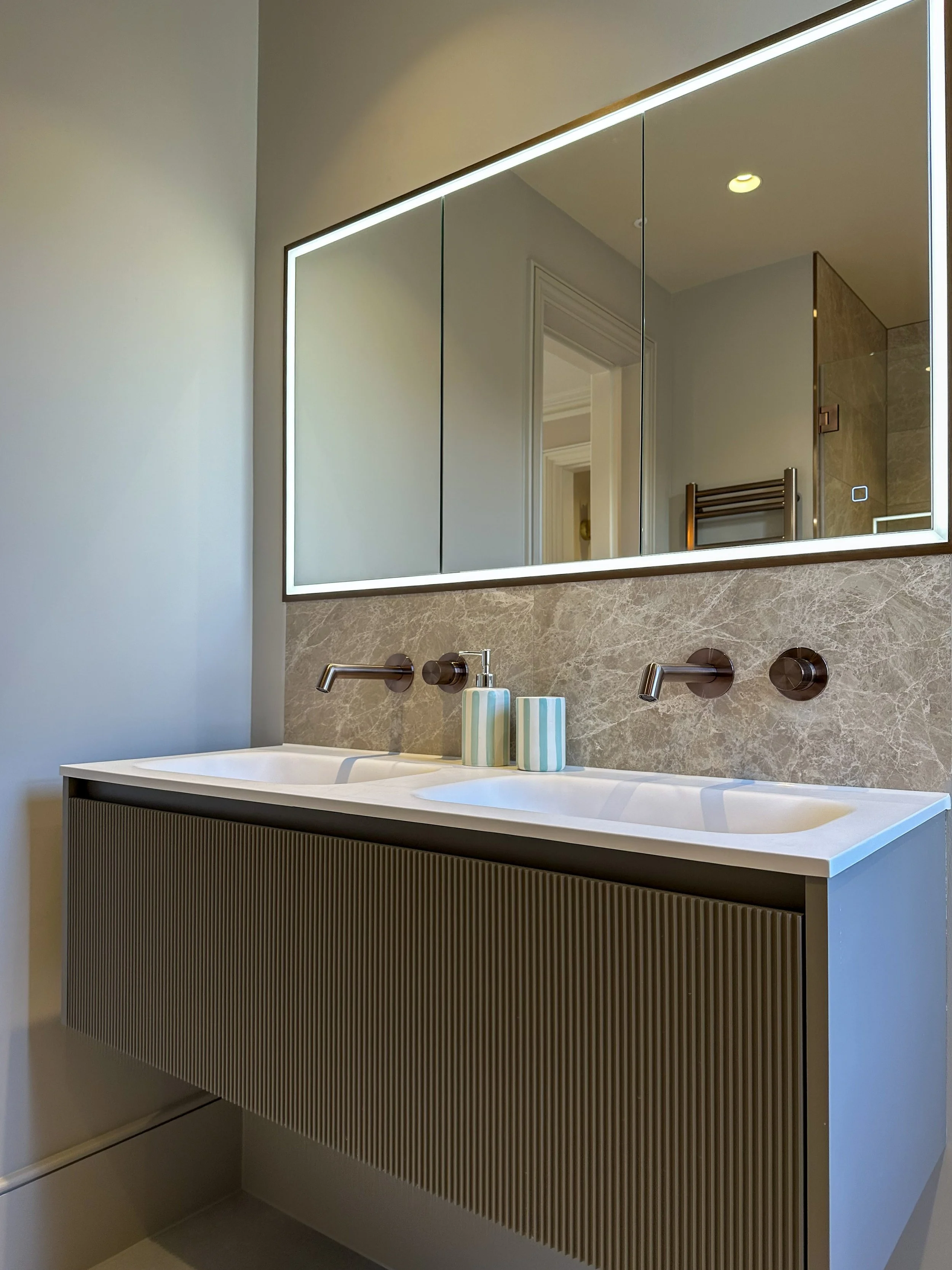 Modern bathroom with a double sink vanity, large illuminated mirror, and neutral-colored decor.