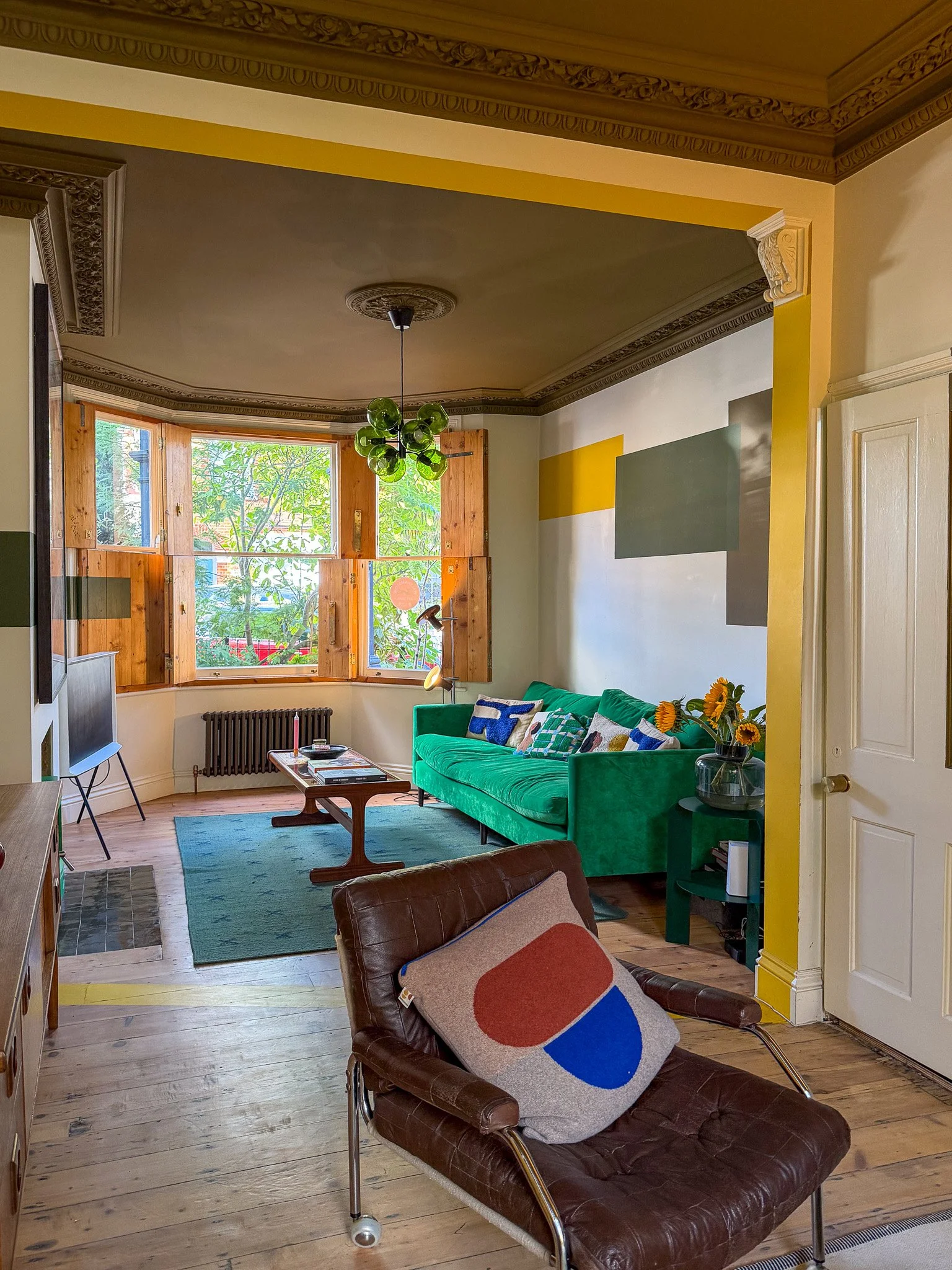 colourful living room with bay window, green sofa, yellow accents and a large bay window with shutters