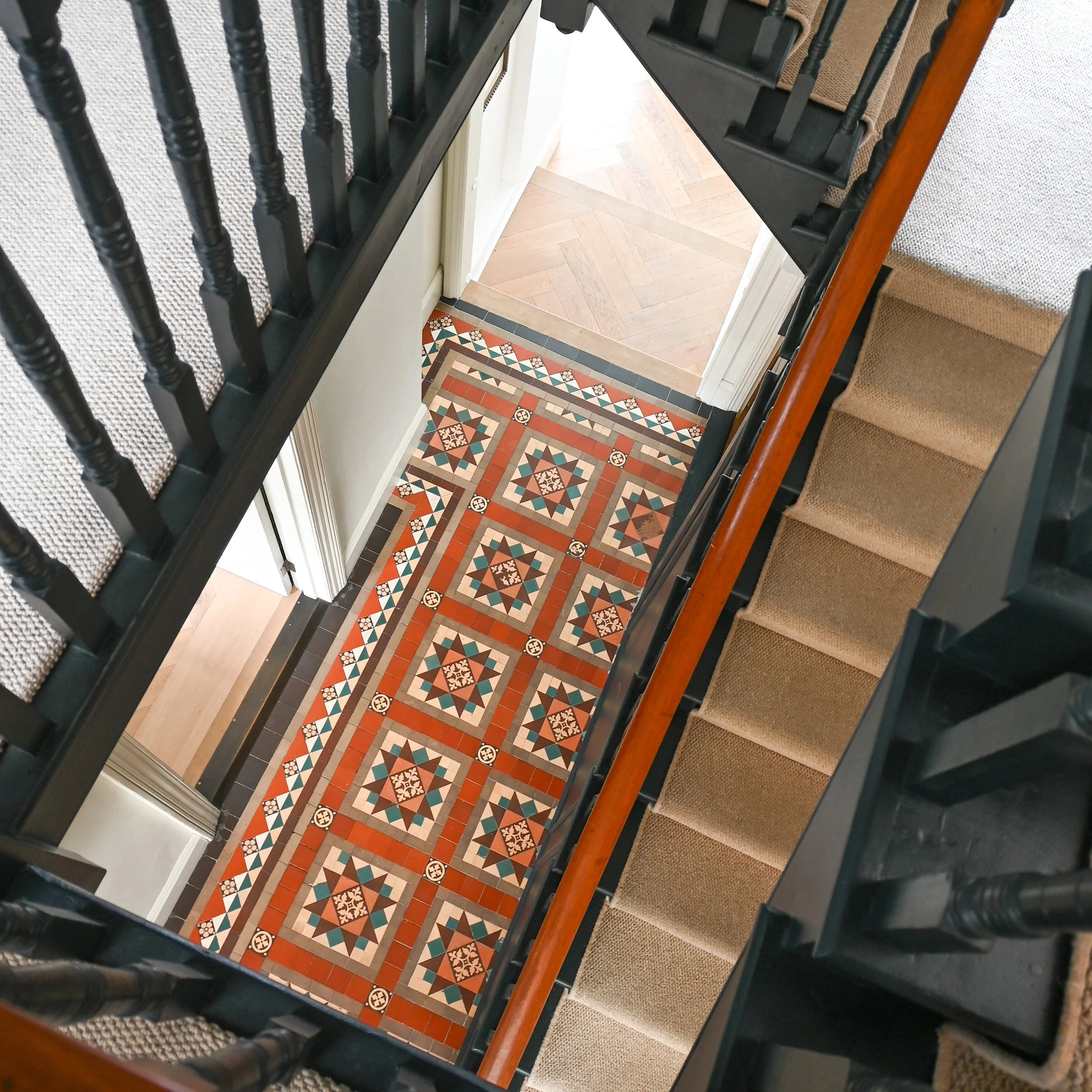 View of a staircase with decorative ceramic tile on the landing, wooden handrails, and black metal balusters, in an indoor setting.