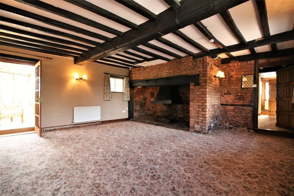 living room with a big dark fireplace, old carpet and dark beams above