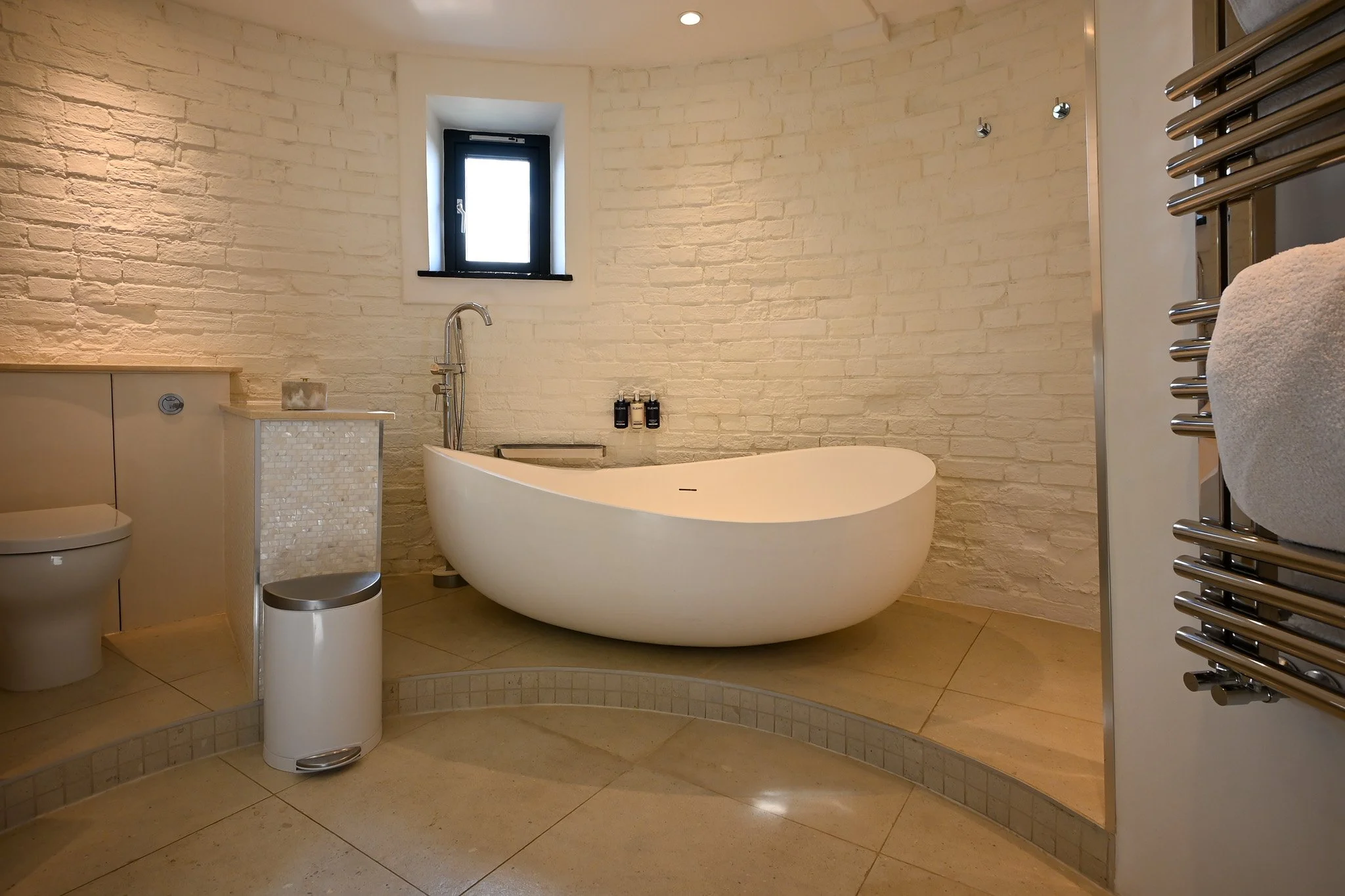 circular bedroom with a large freestanding bath tub, brick walls and tiled flooring