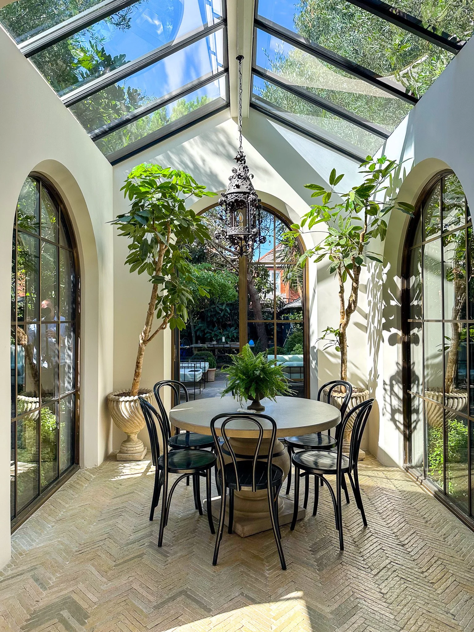 dining table with orangery style extension with plants and rooflights on tiled floor and double arched doors