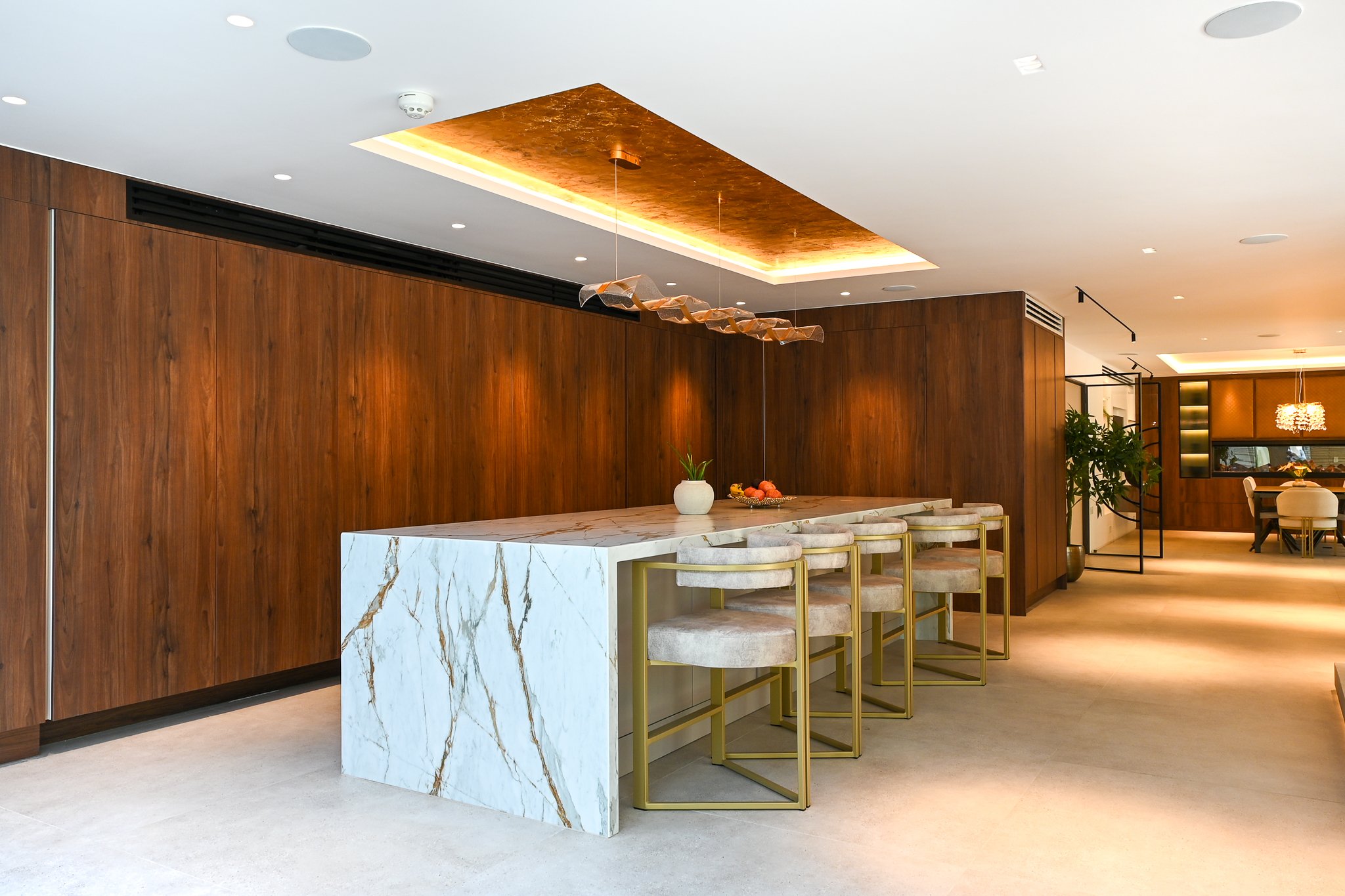 Large kitchen island with marble worktop and wooden finished cupboards with a central hanging light
