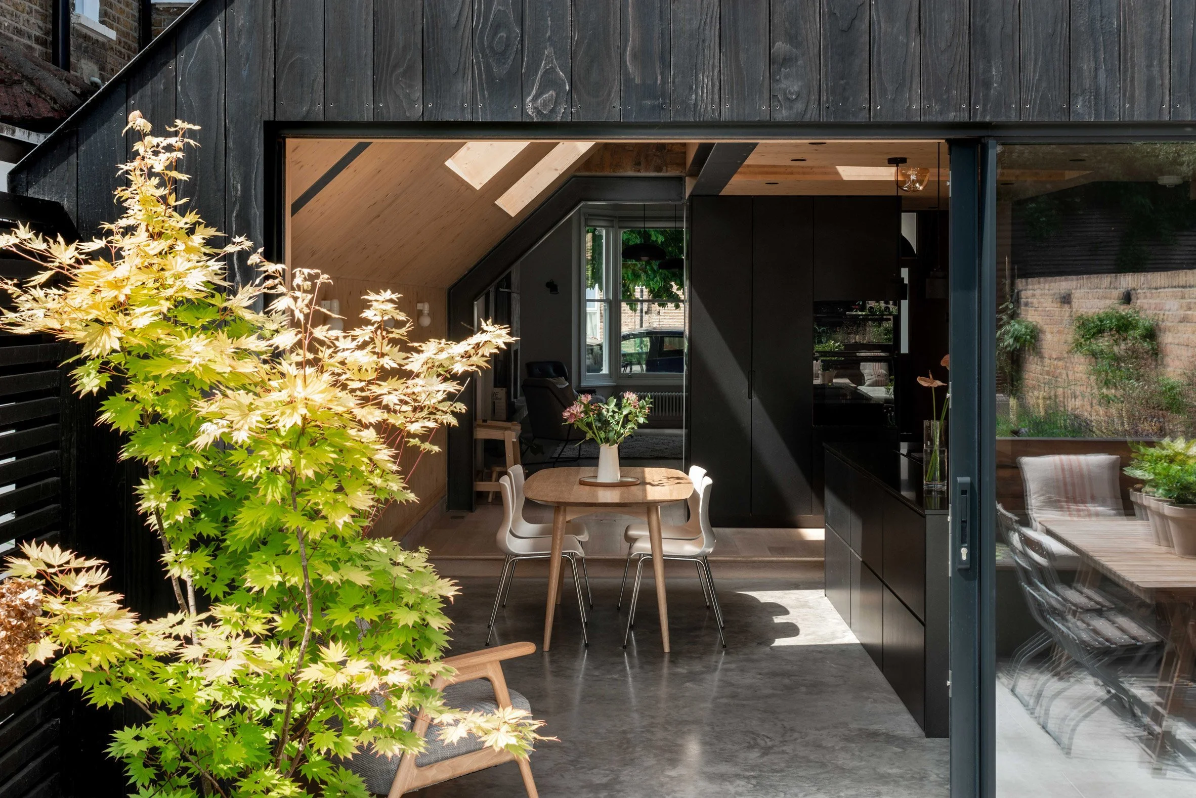 Interior view of a modern home with a dining area and a view into a cozy living space, featuring black cabinetry, wooden accents, and a large window with natural light.