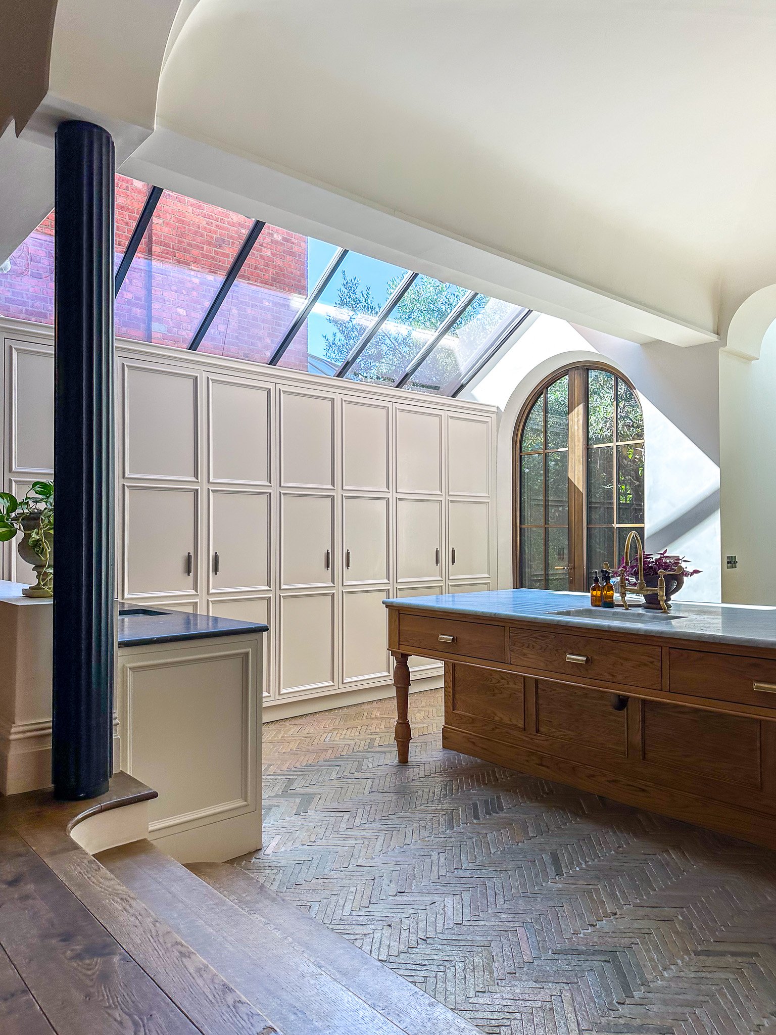 wooden kitchen island with tiled flooring and wall cupboards by arched window