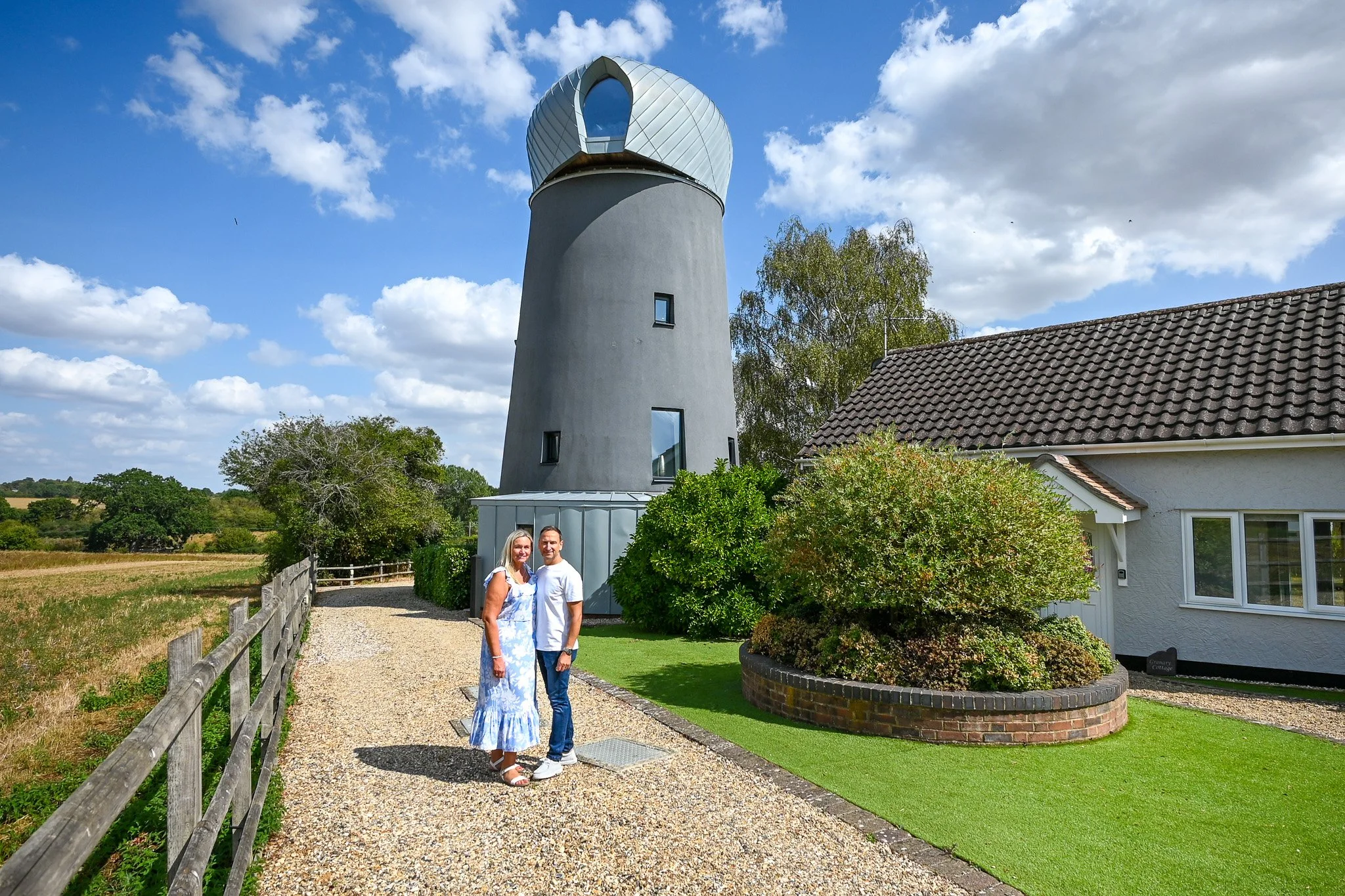 couple standing on gravel driveway by their converted windmill with zinc roof