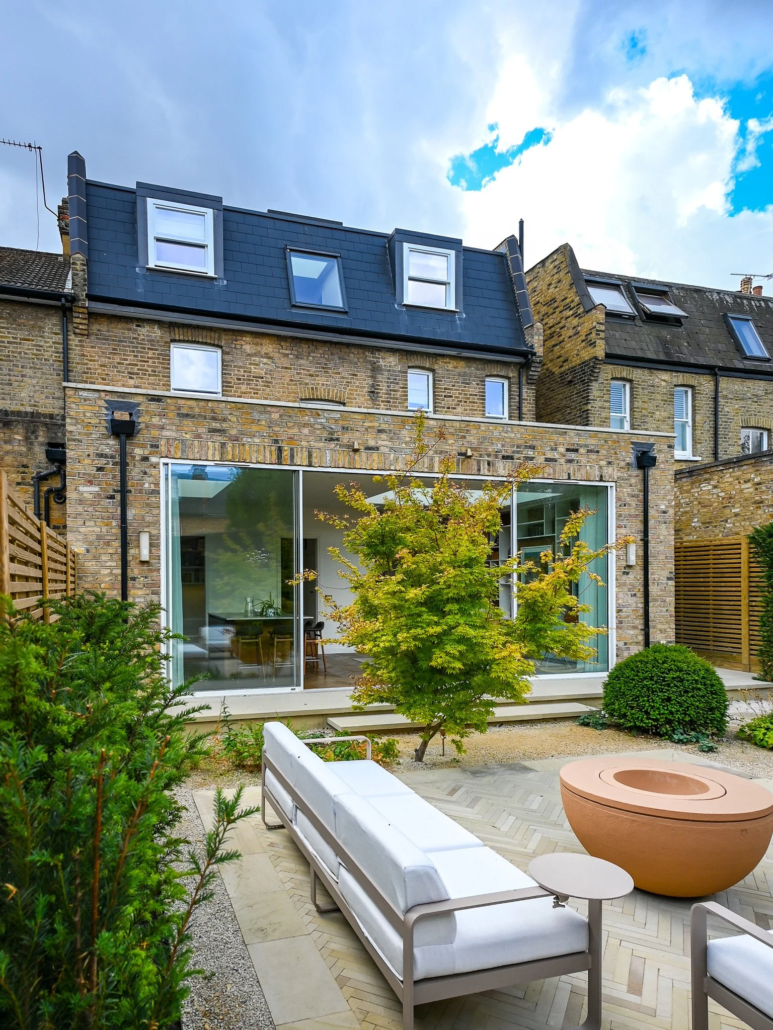 large victorian home with a rear extension and loft conversion with two dormers, and a rear garden with a sofa and trees