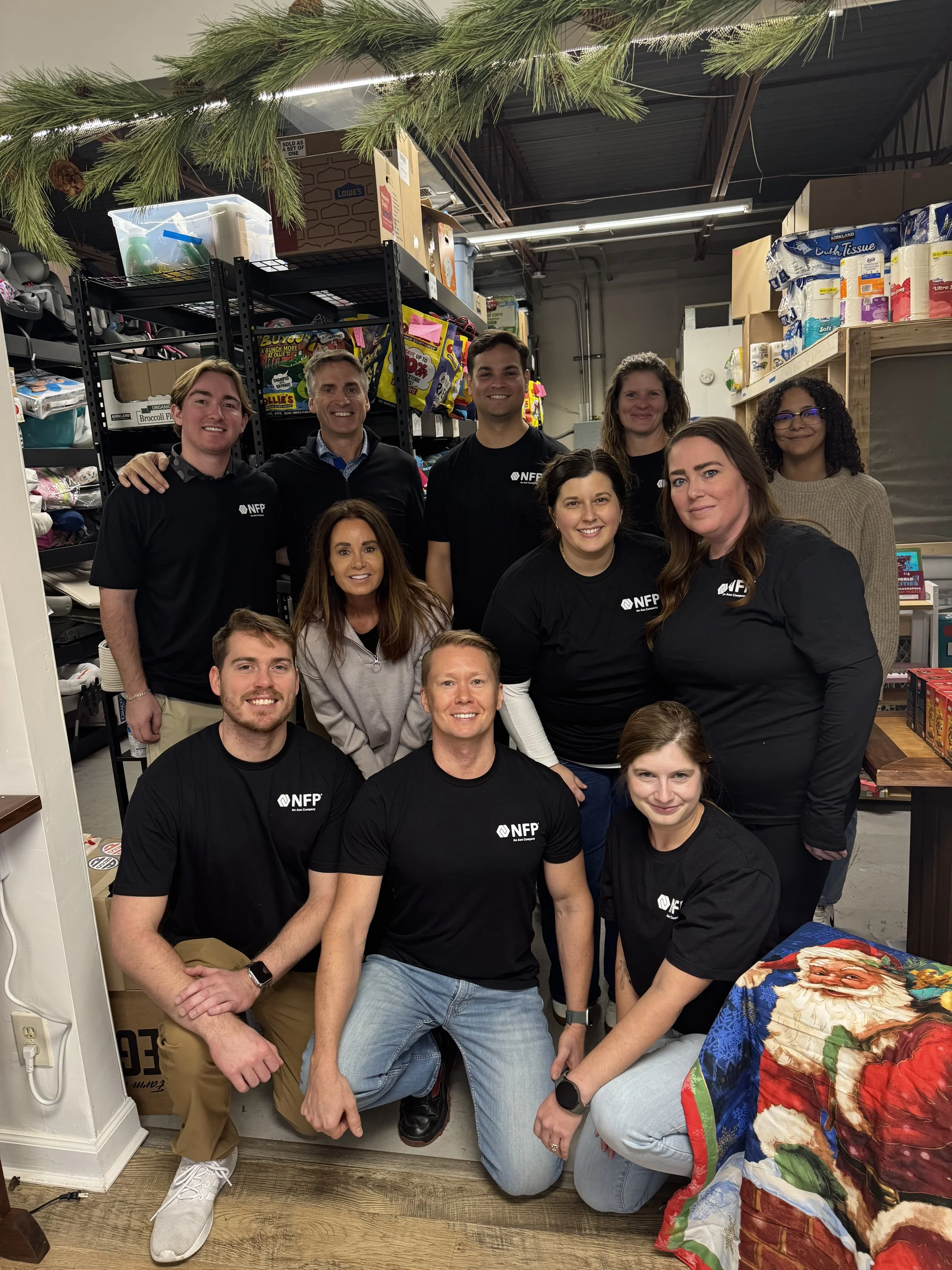 Group of twelve volunteers posing together in Helping Hand Me Downs' warehouse, where they pack clothes for St. Louis area families in crisis.