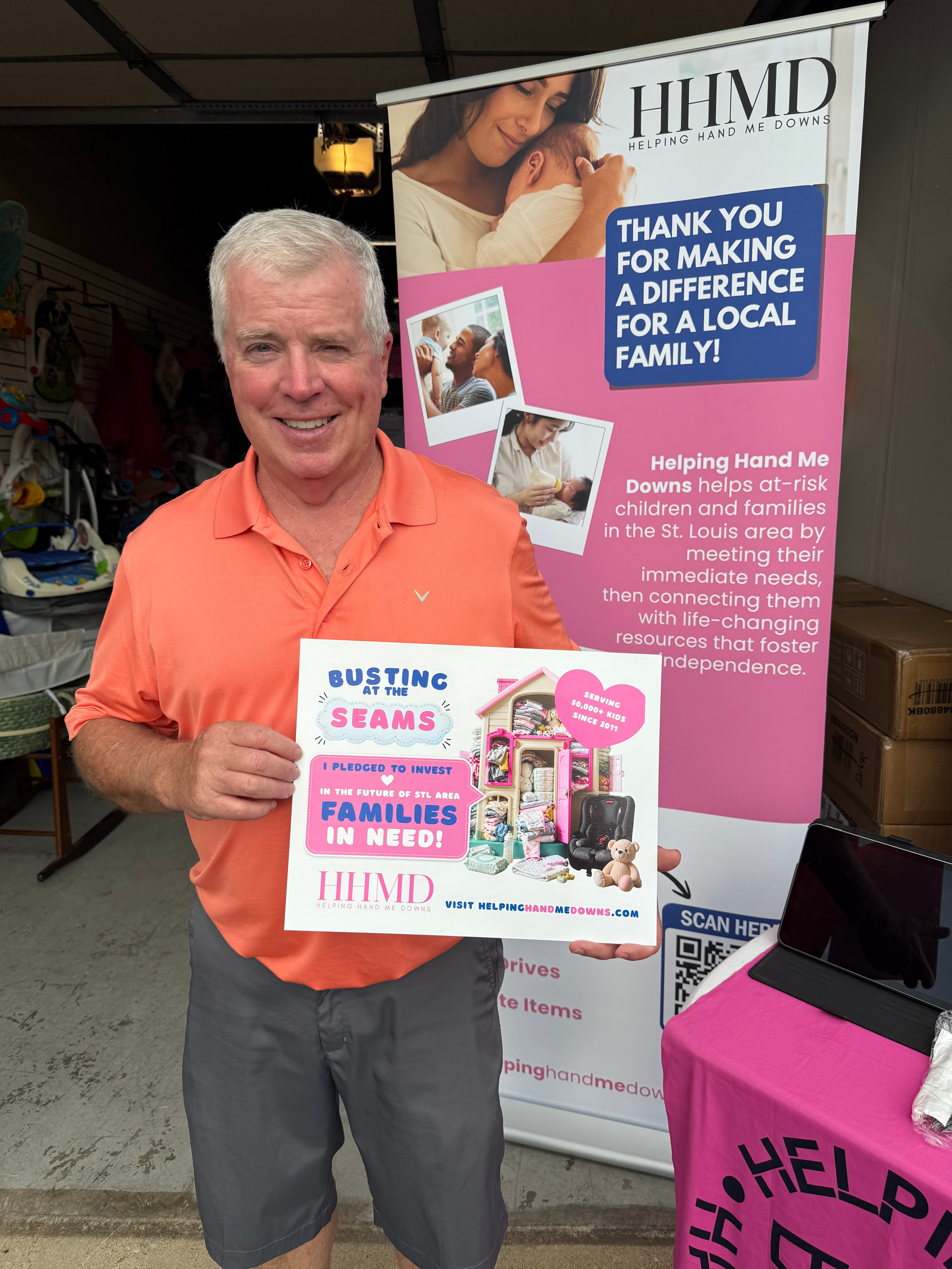 A man with short gray hair, wearing an orange polo shirt and gray shorts, holding a flyer at a charity event.