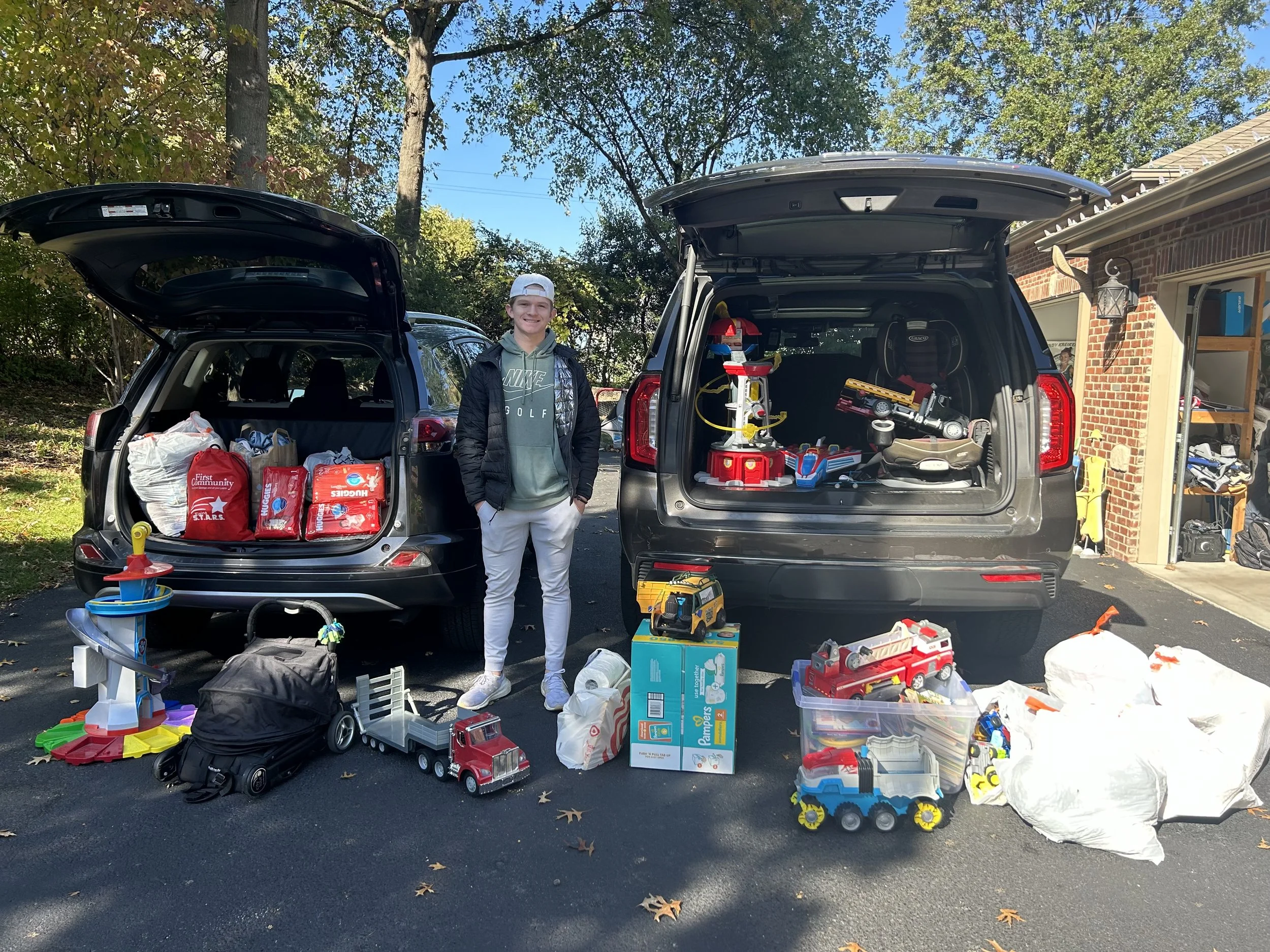 A large donation dropped off at Helping Hand Me Downs as a volunteer unloads two open cars filled with toys, bags, and supplies.