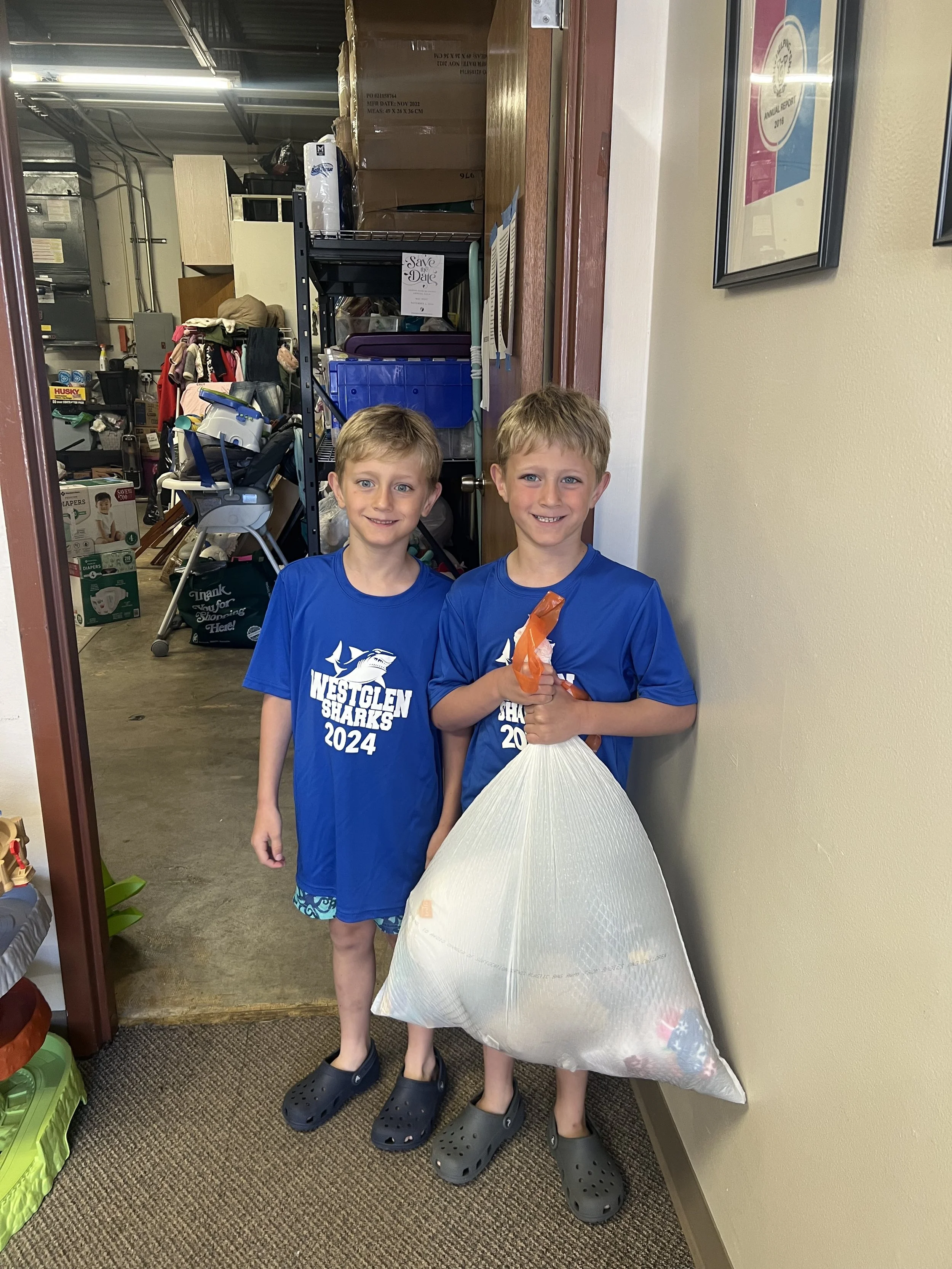 Two young boys volunteering at Helping Hand Me Downs by donating their clothes, sorting their donations and packing bags for St. Louis families in need.