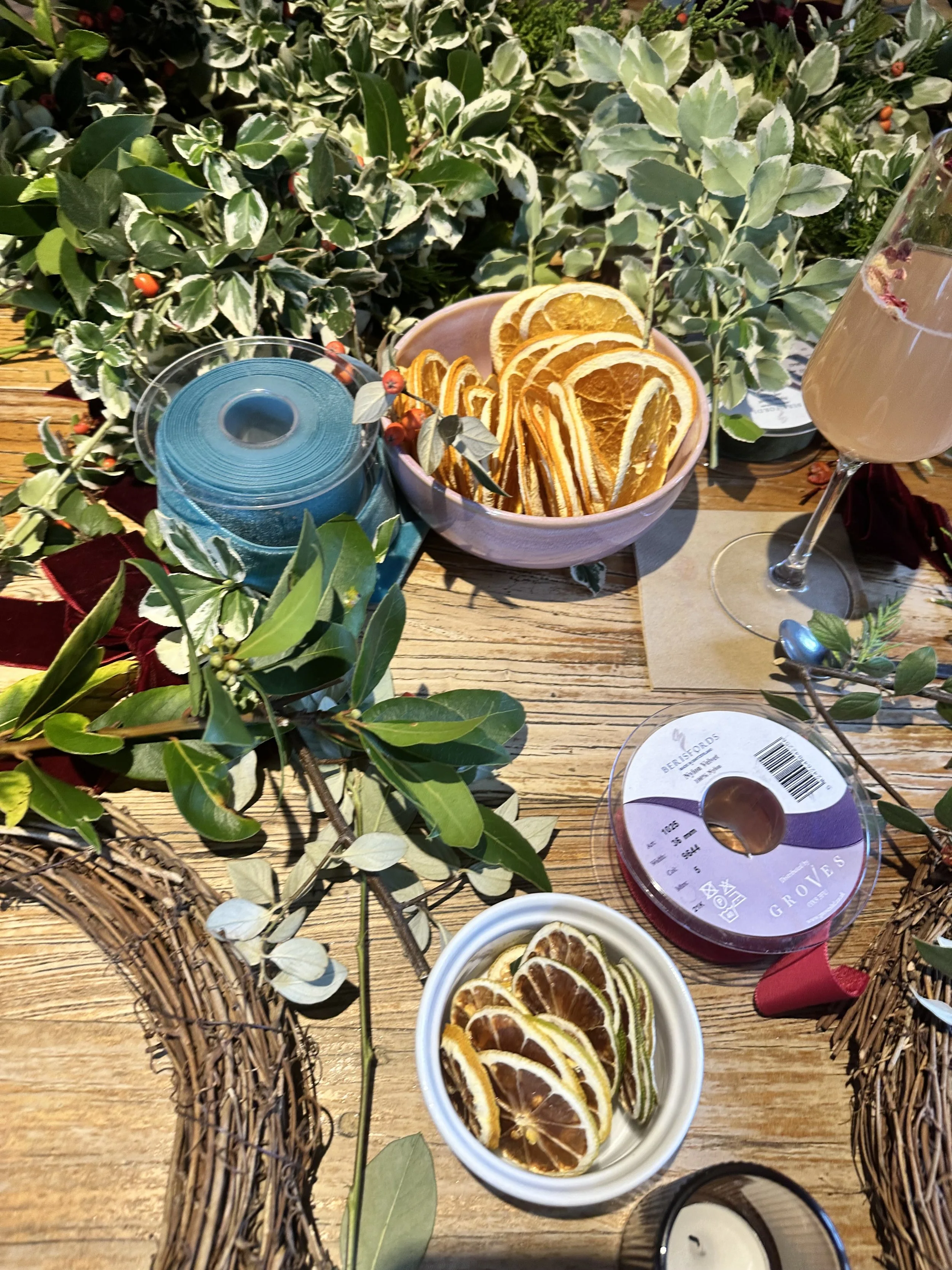 A decorated table with bowls of sliced dried oranges, a candle, greenery, and a glass of drink.