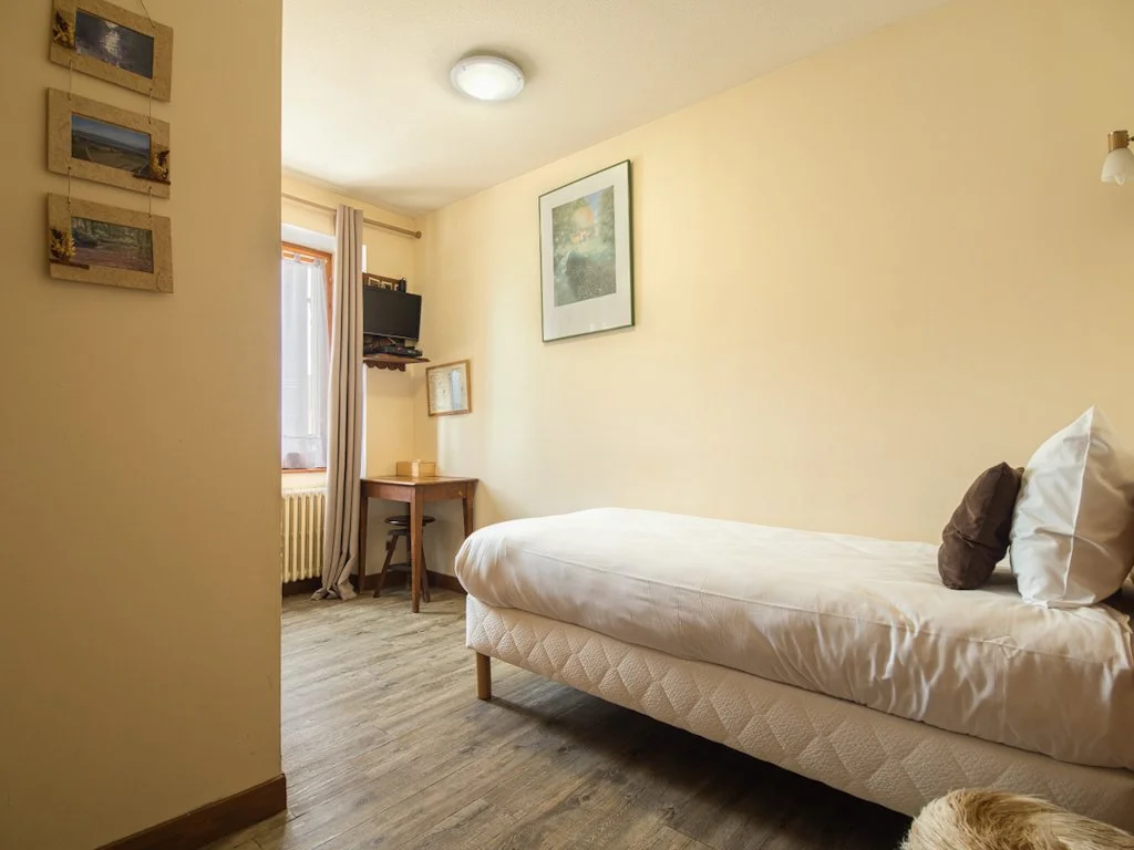 Chambre simple avec lit, table à côté de la fenêtre, télévision murale, et décoration murale