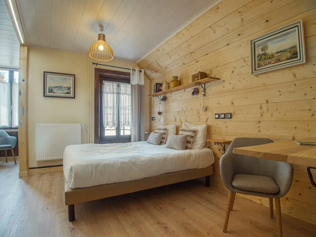 Chambre avec lit double, mur en bois, fenêtre avec rideaux, bureau avec chaise, lampe suspendue