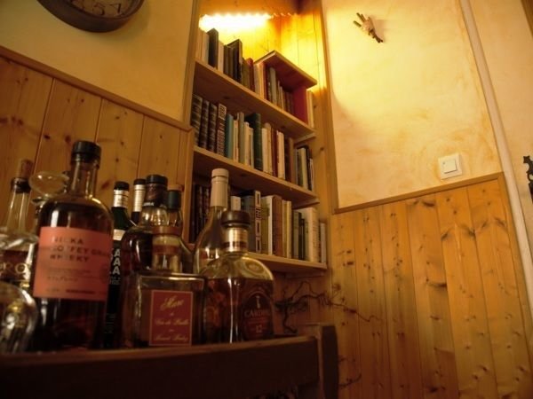Une bibliothèque avec des livres rangés sur des étagères en bois, et plusieurs bouteilles en verre sur une surface en bois au premier plan.