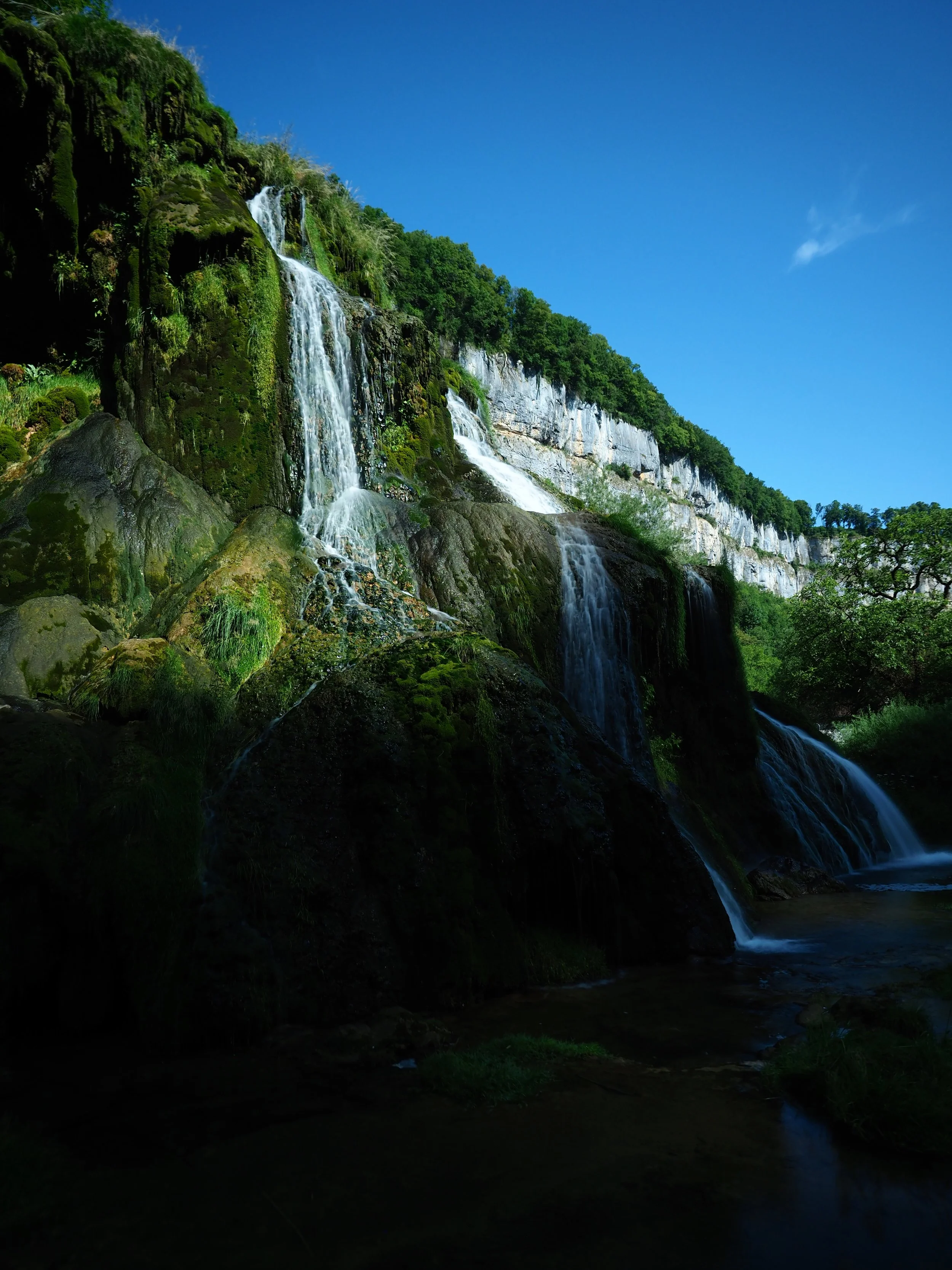 Cascade d'eau dans une forêt verte sous un ciel bleu.