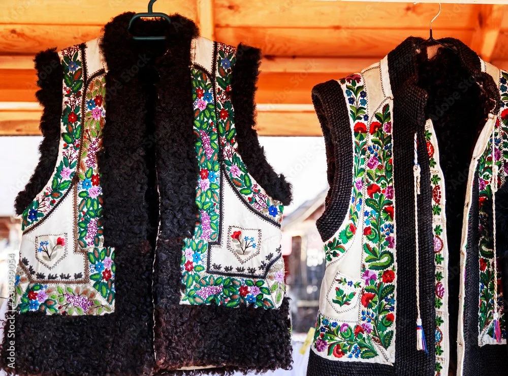Two traditional embroidered vests with floral patterns hanging on hangers.
