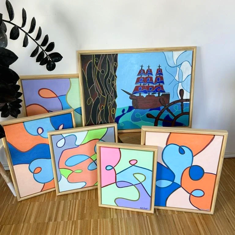 Mehrere bunte, abstrakte Gemälde in Rahmen, eines zeigt ein Segelschiff auf dem Wasser, die anderen bestehen aus organisch wirkenden Linien und Flecken in leuchtenden Farben.