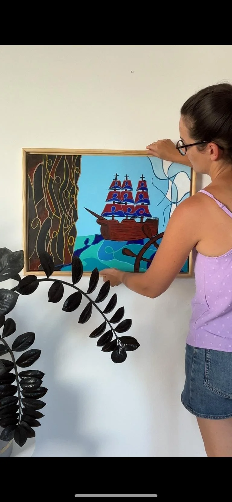 Frau hängt ein Gemälde eines Segelschiffs an einer weißen Wand auf.