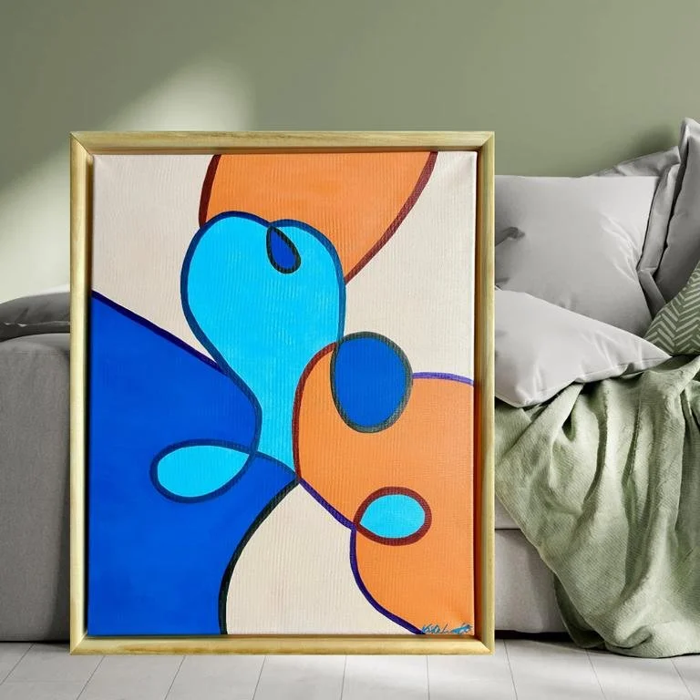 Abstraktes Gemälde mit blauen, orangefarbenen und schwarzen Linien auf Leinwand, im Holzrahmen, vor einem grauen Sofa mit Kissen und Decke. Gemalt mit Acrylfarben und Metallicstiften.