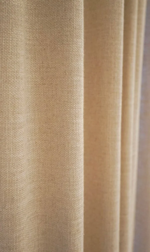 Close-up van beige gordijnstof met textuur en plooien.