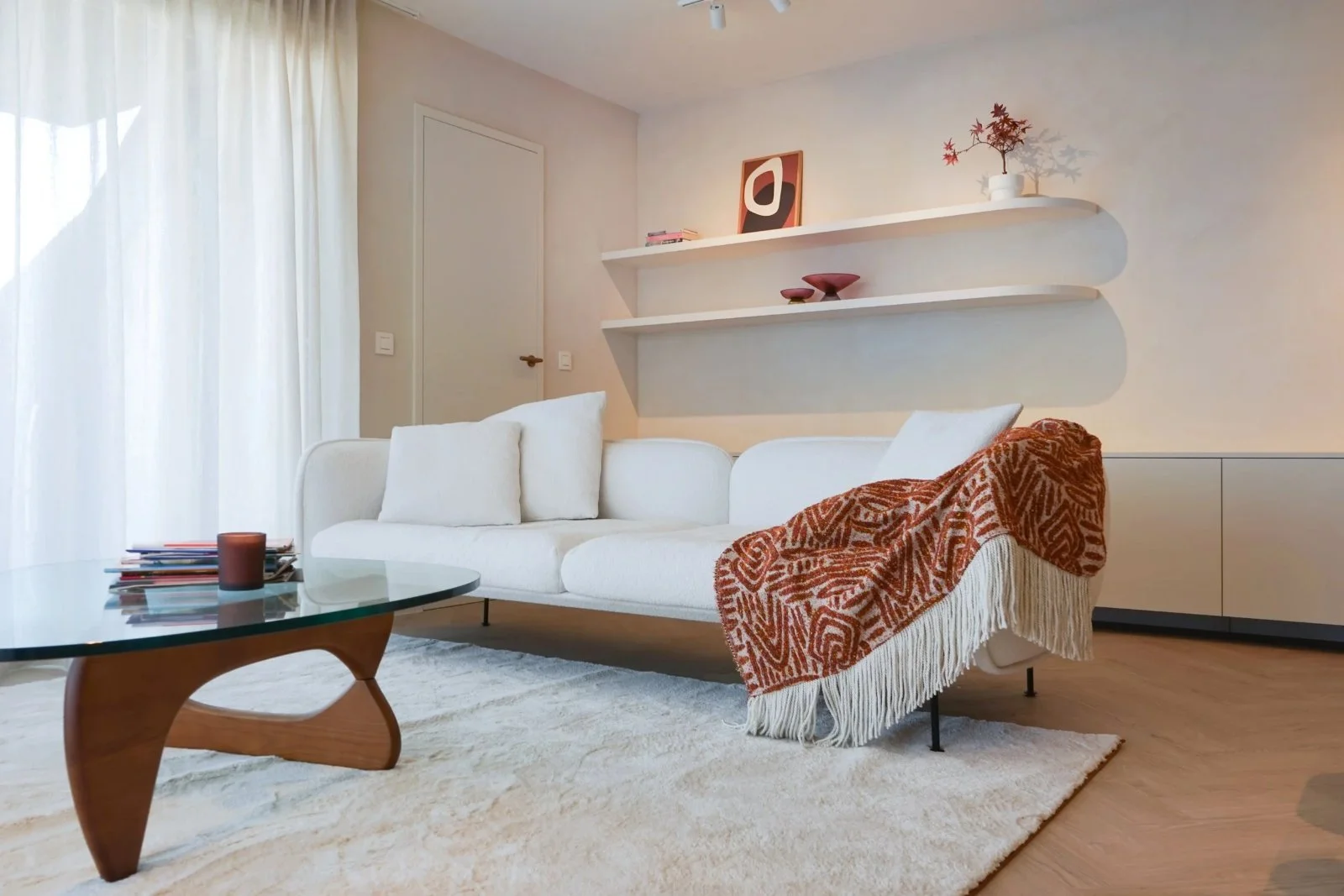 Lichte woonkamer met wit zitmeubel en warme houten accenten, gerenoveerd appartement aan zee door Atelier Ombre