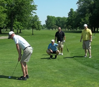 Four people playing golf on a lush green golf course, with trees in the background. Golf 4 Life, Shelby County Ohio Right to Life.