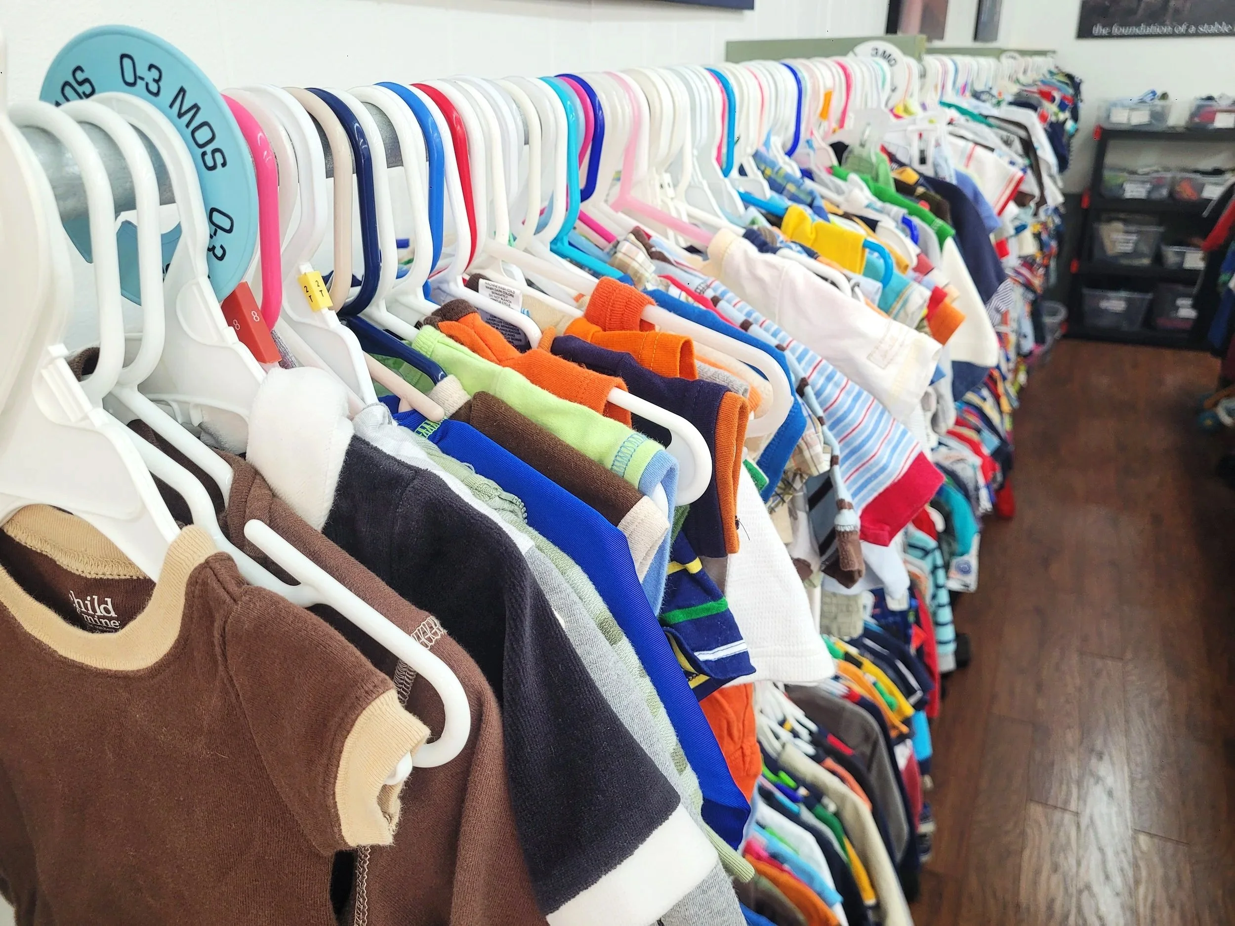 Clothing rack filled with children's shirts and sweaters on white and colored hangers in a thrift store.