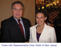 A man in a dark suit with a striped tie and a woman in a white blazer smiling together indoors.