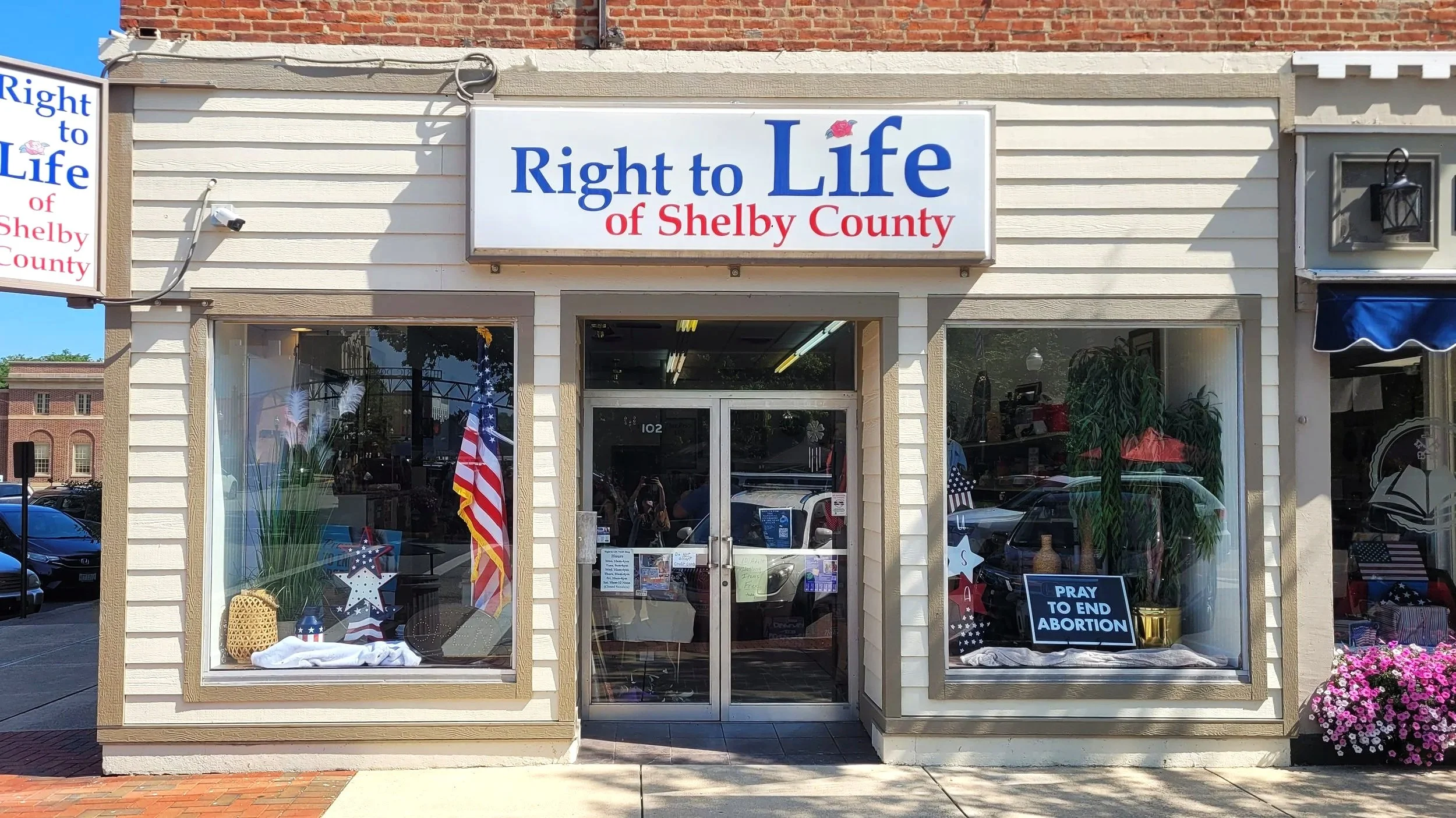 Storefront with sign that reads 'Right to Life of Shelby County'; window displays patriotic decorations and a sign saying 'Pray to End Abortion'.