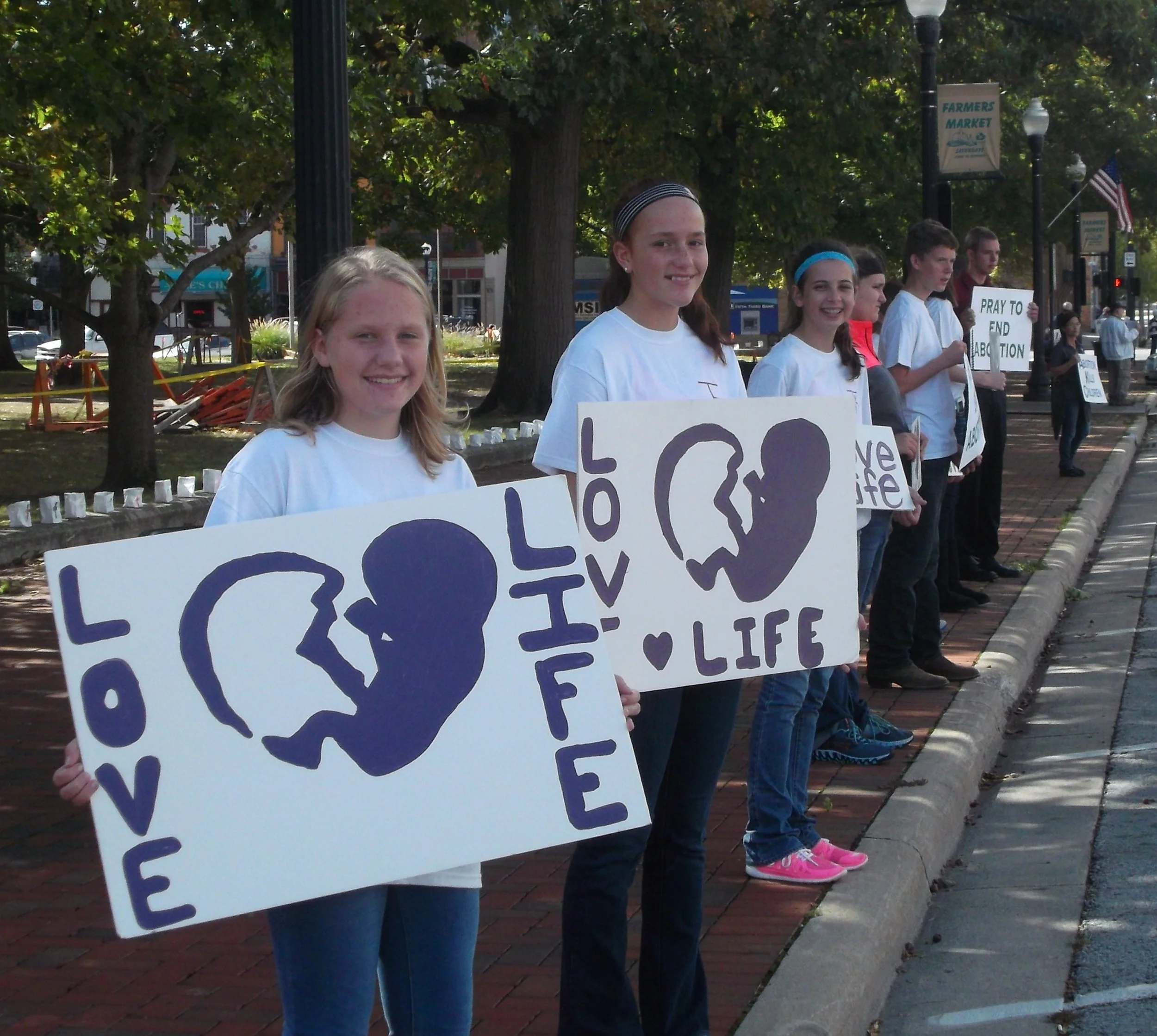 Group of young people standing on a sidewalk holding signs with a blue silhouette of a fetus and the words "LOVE LIFE."