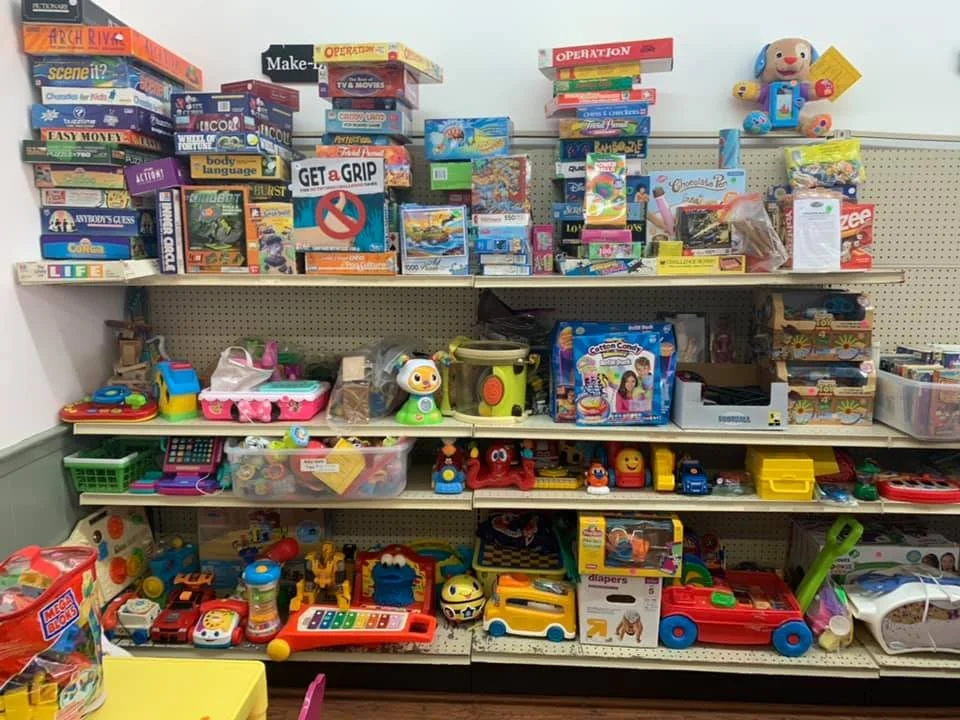A store shelf filled with various children's toys including board games, plush toys, toy cars, and educational toys displayed on three levels.