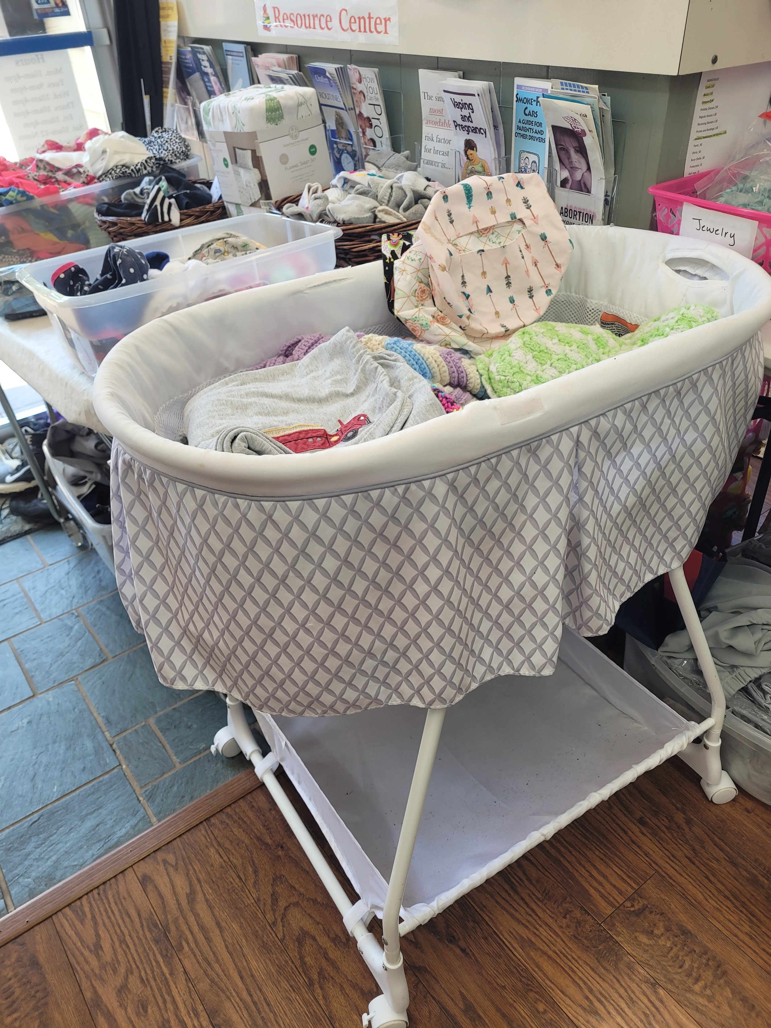 A baby changing table with a patterned fabric cover, filled with clothes and baby items, in a resource center or thrift store setting.