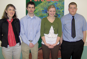 Four young adults standing in front of a colorful painting, posing for a group photo indoors.