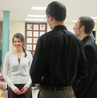 A woman and two men in a room with framed pictures on the wall, smiling and conversing.