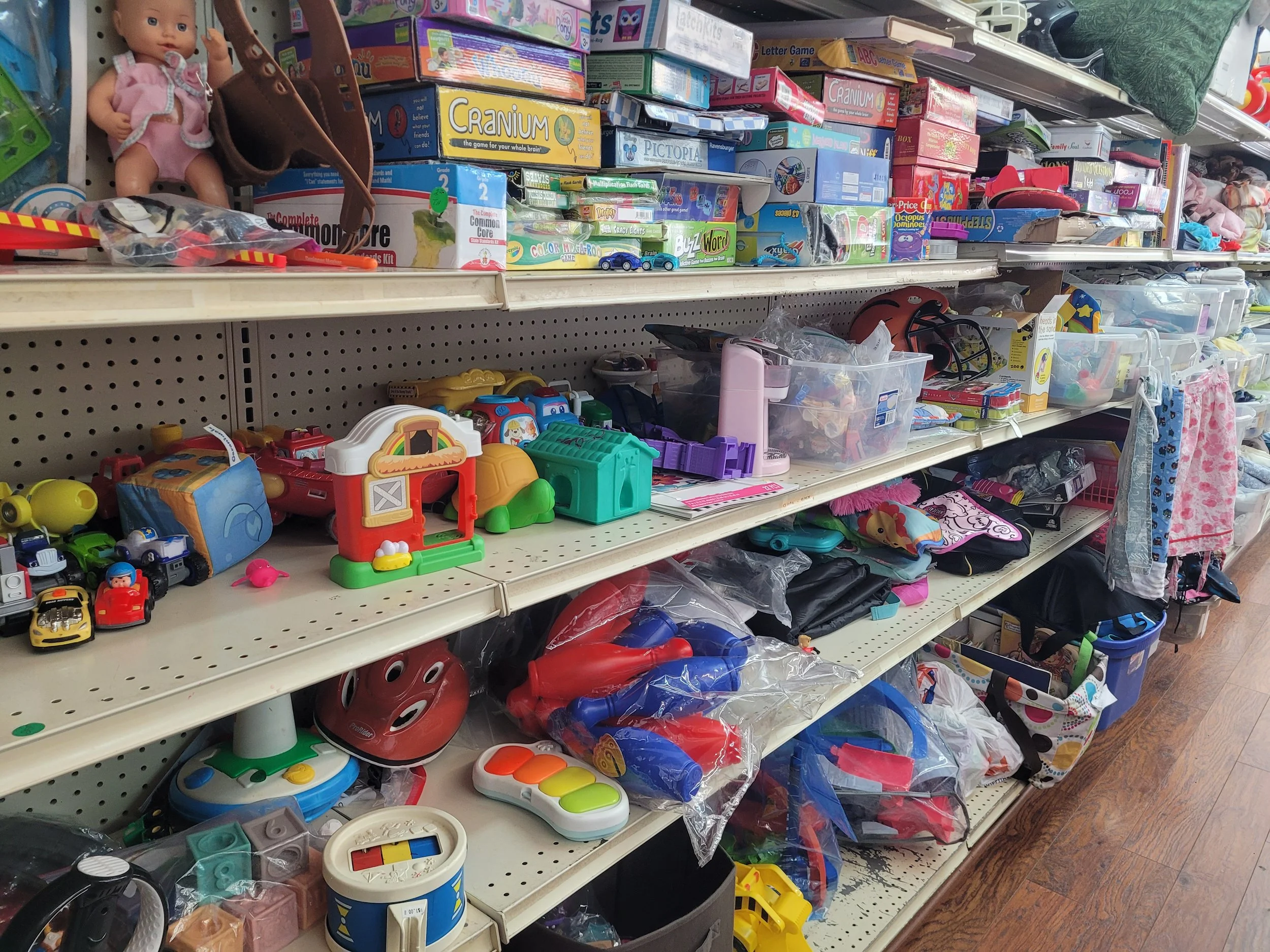Toy aisle with various children's toys including riding toys, dolls, toy vehicles, and games on shelves in a store.